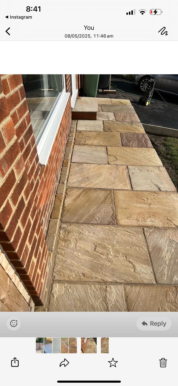 Stone patio walkway beside a brick house, with a window and black railing.