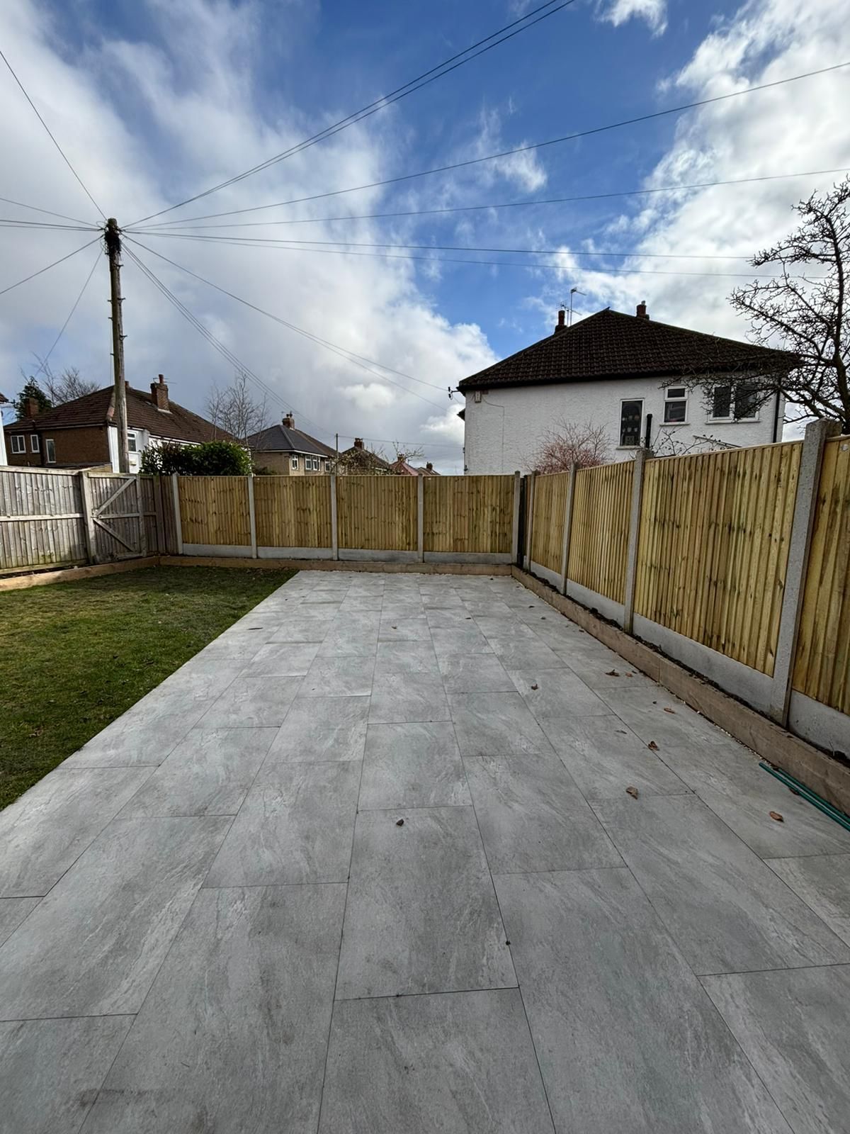 Concrete driveway leading to a wooden fence and white house under a cloudy sky
