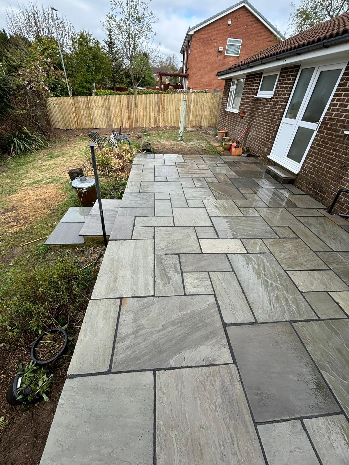 Newly paved gray stone patio beside a brick house and garden fence