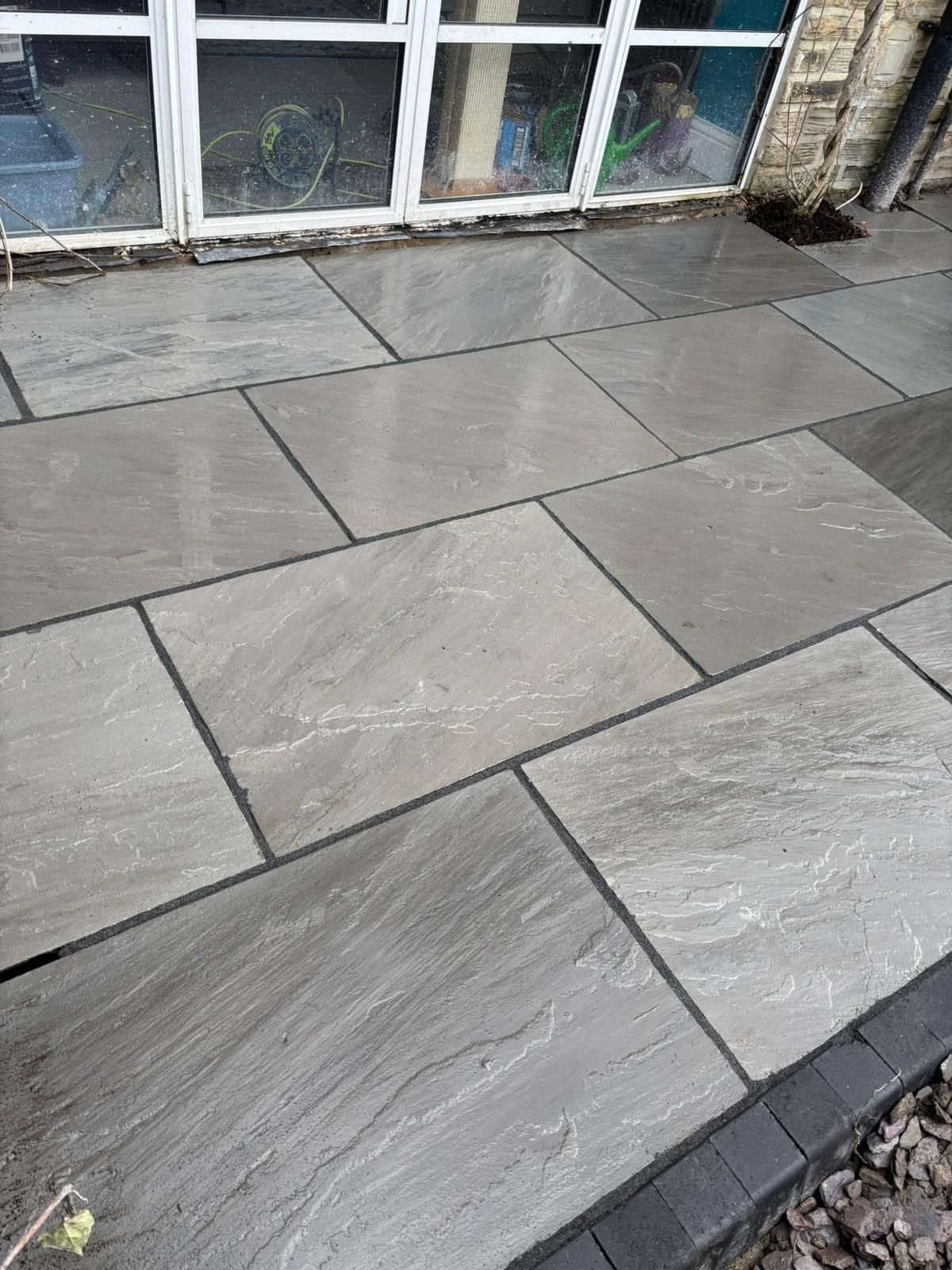 Gray stone patio paving in front of a windowed storefront, with a pebble border along the edge