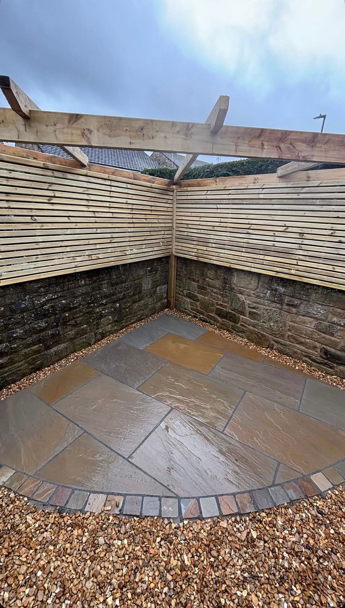 Corner outdoor garden seating area with woven fence, stone pavers, and gravel ground
