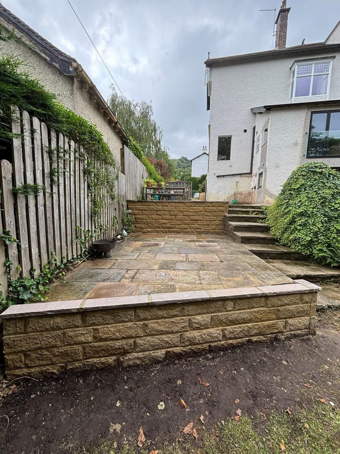 Stone patio courtyard with steps beside a white house and ivy-covered wall under cloudy sky