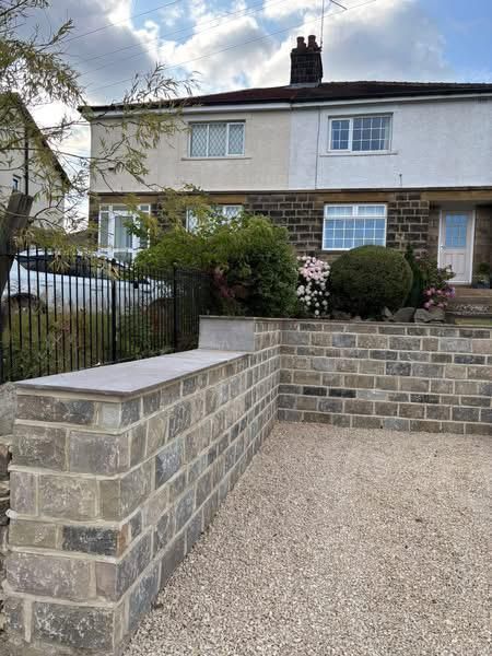 Stone-front house with gravel drive and low brick retaining walls in a front garden