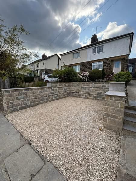 Stone-front house with a gravel driveway bordered by low brick walls under a cloudy sky
