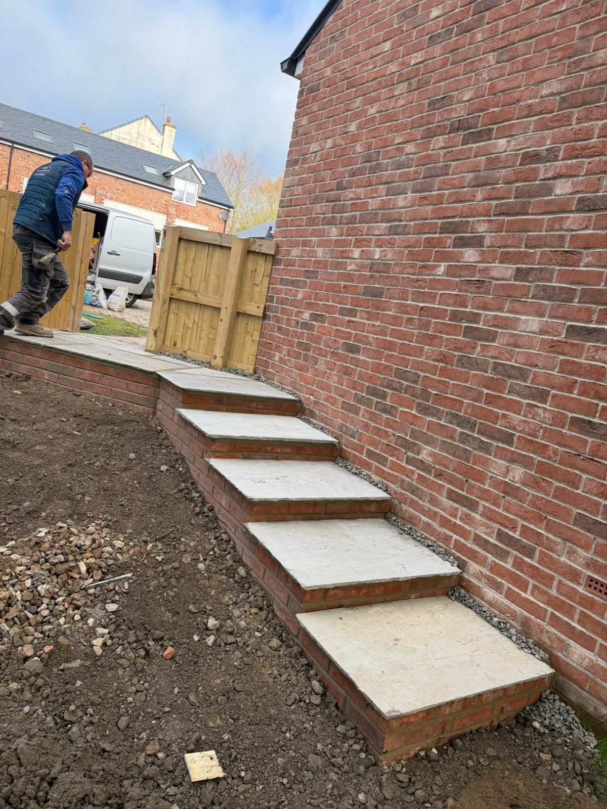 Outdoor steps under construction beside a brick wall, with a worker in the background