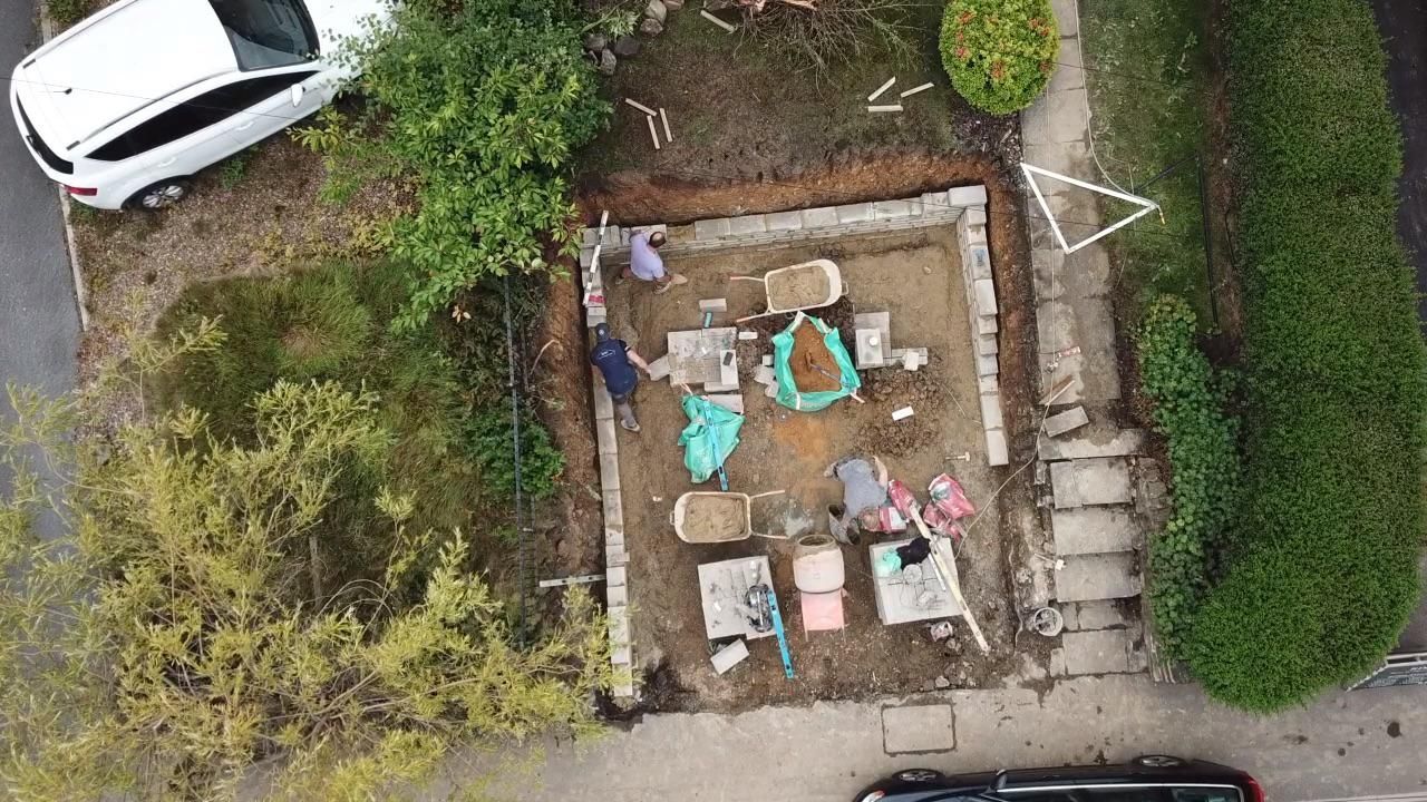 Aerial view of a small brick-lined garden with a patio table, chairs, plants, and parked cars nearby.
