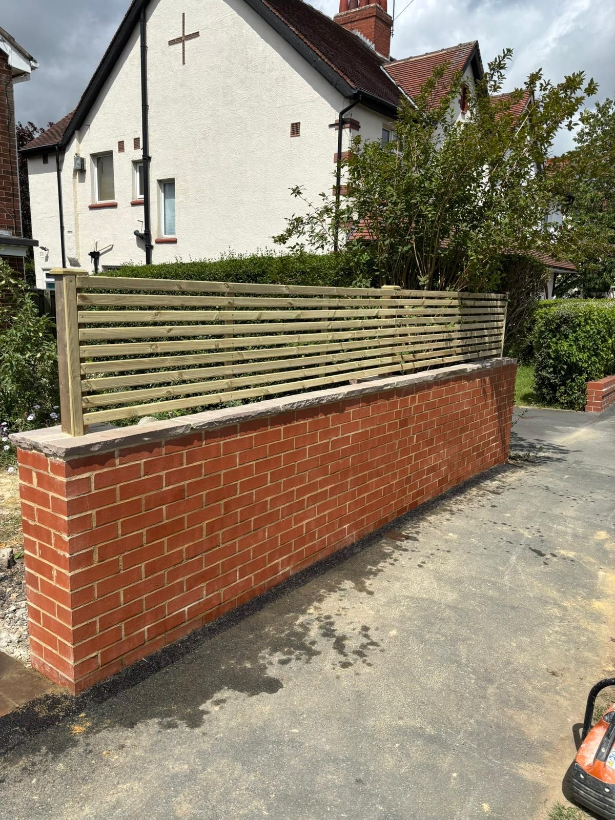 Brick retaining wall with wooden fence beside a driveway in front of a white house