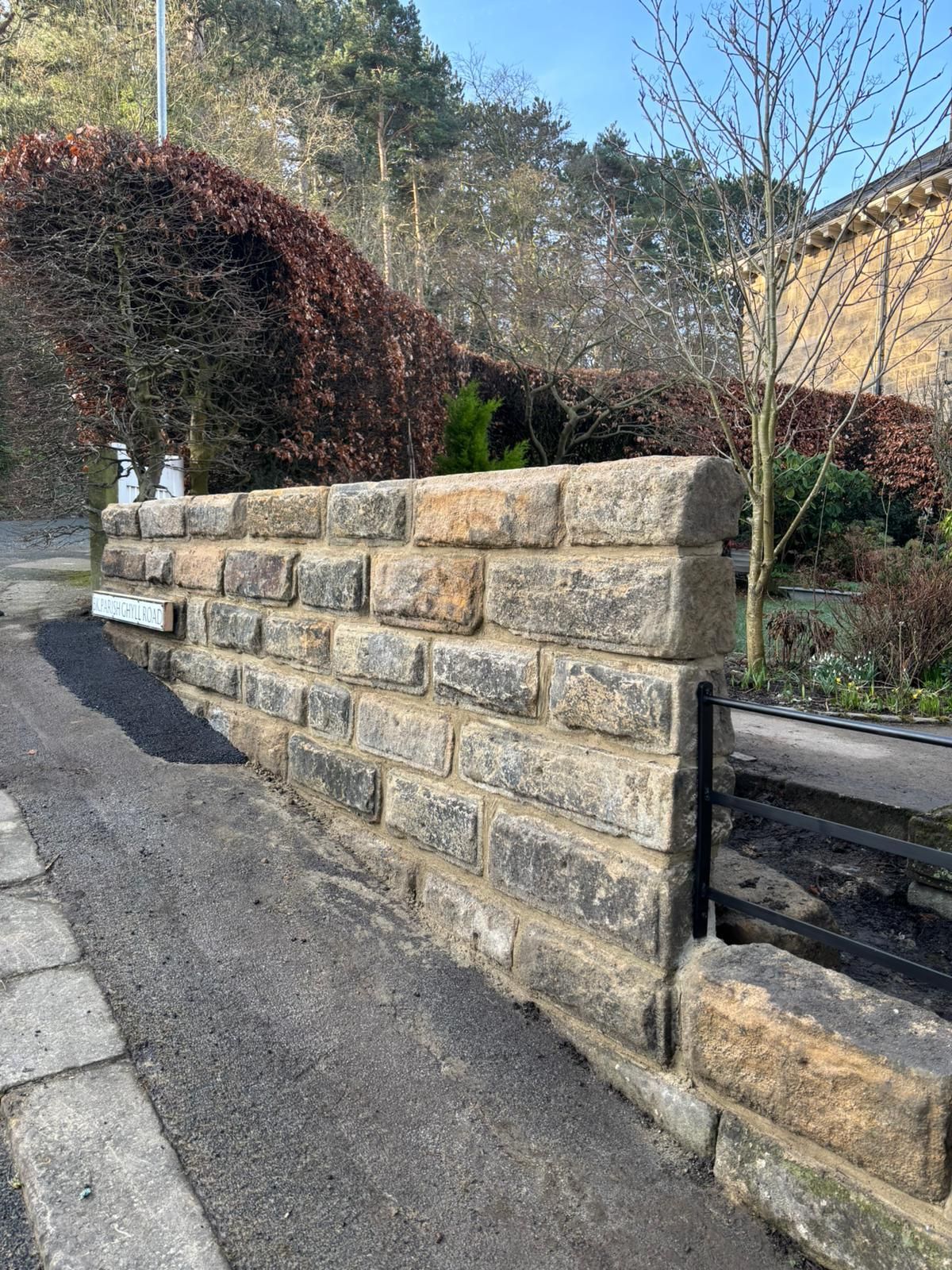 Stone retaining wall along a sloped driveway beside a garden and house