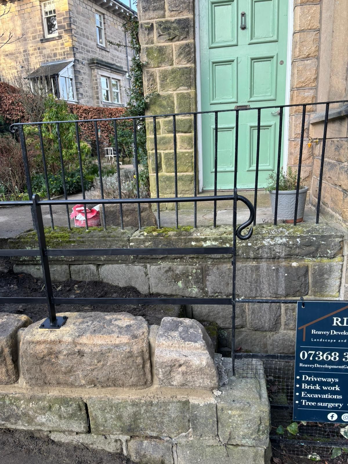 Stone steps and black railings leading to a mint-green door on a stone building, with a sign at right.