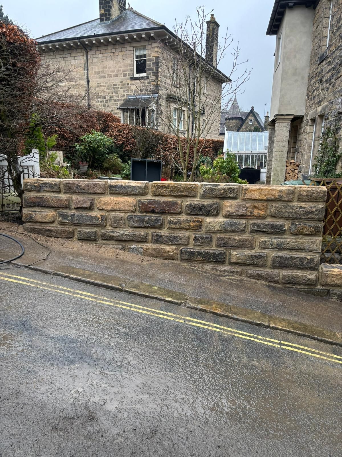 Stone wall and wet street between old stone buildings in a narrow village lane
