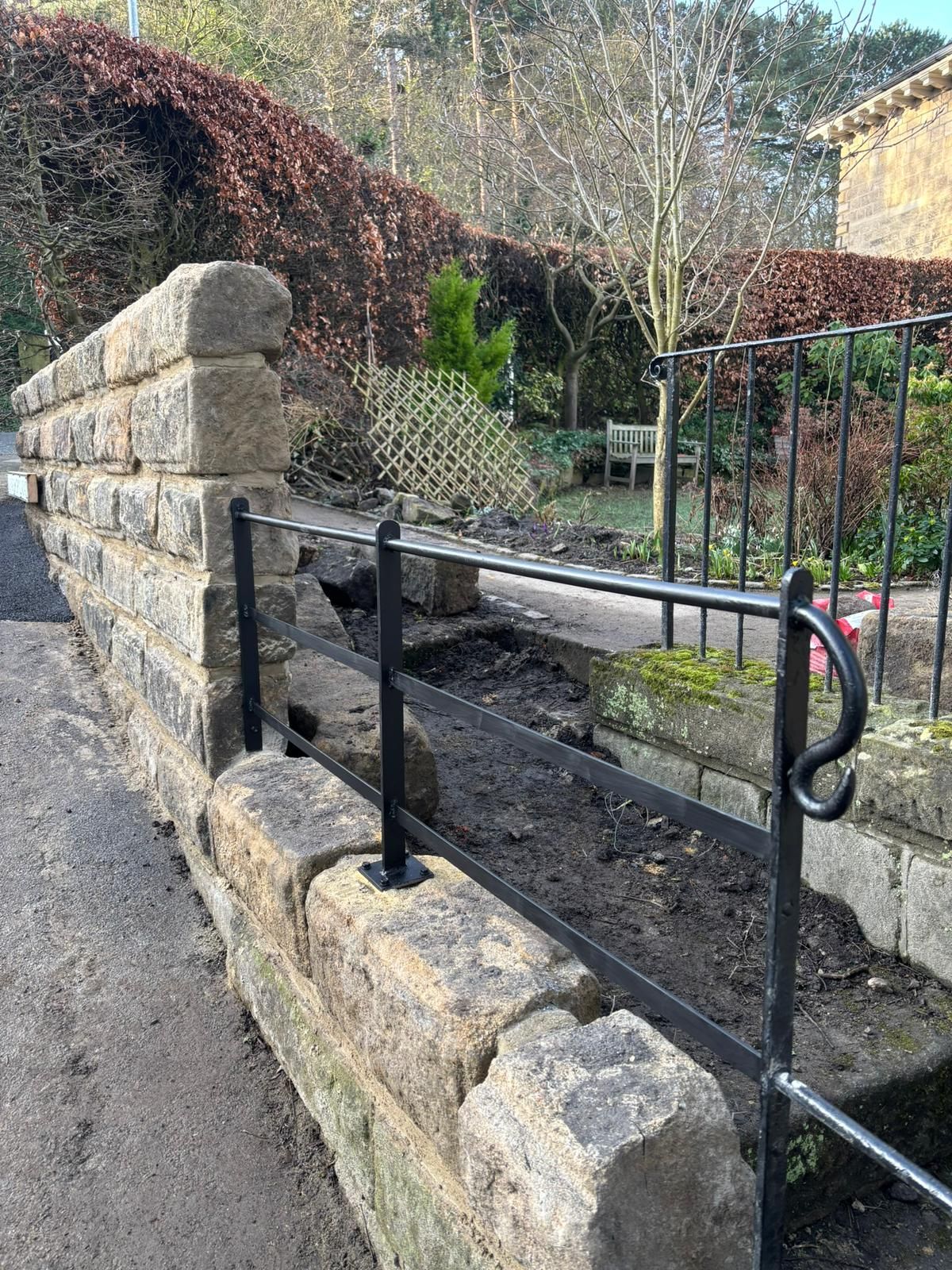 Stone steps with black metal railings beside a garden wall and hedge-lined path