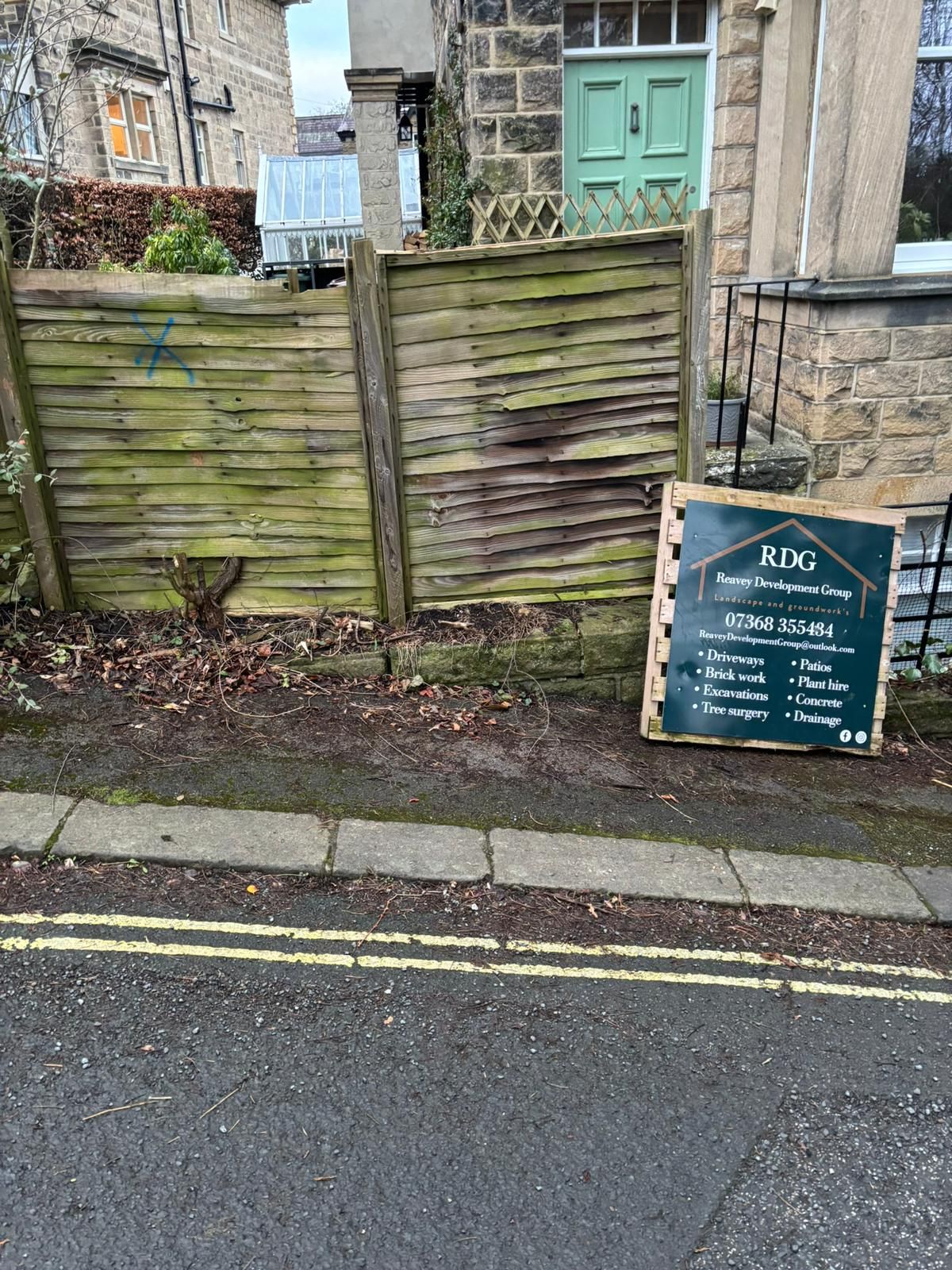 A green wooden gate beside a stone building, with a chalkboard sign on the pavement.