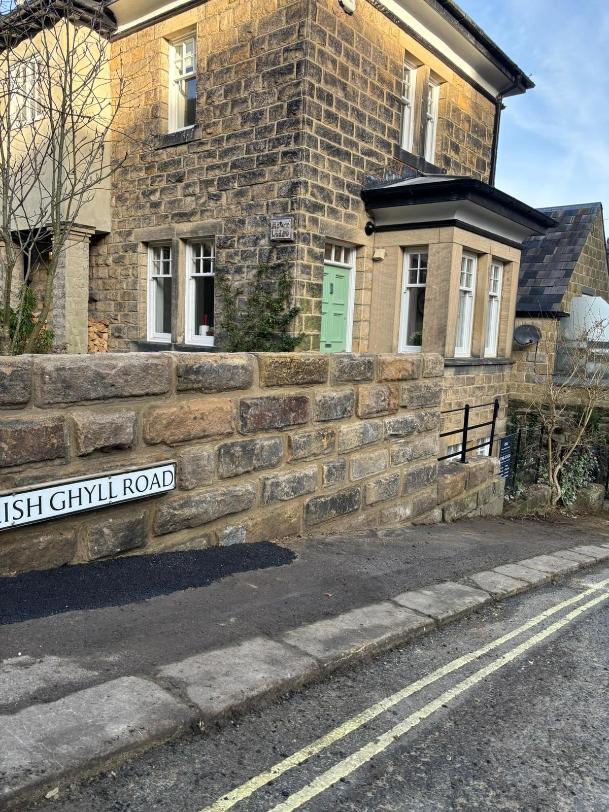 Stone house on a roadside corner with stone wall and green door, under a blue sky.