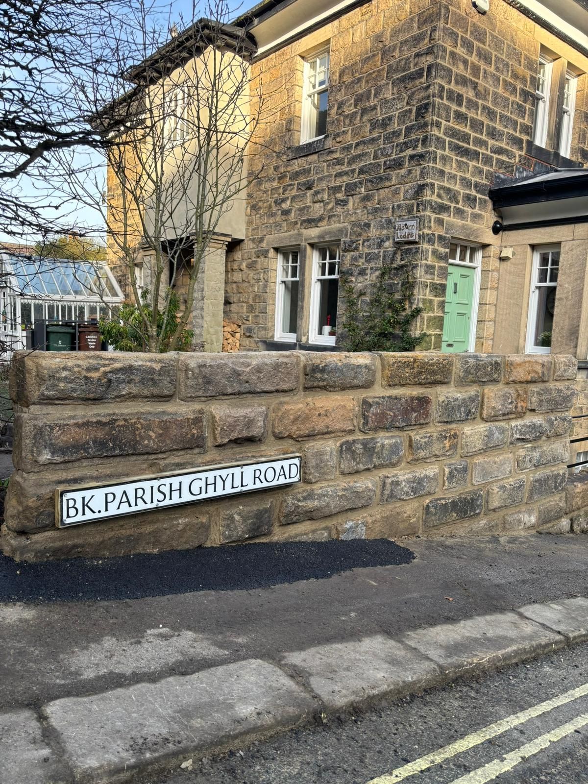 Stone wall and house on a street corner with a sign reading “BK Parish Church Road.”