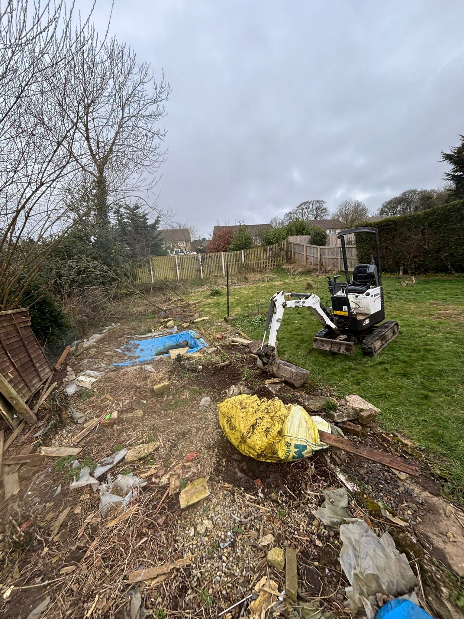 Littered overgrown path with rubble, yellow trash bags, and a black scooter under a gray sky.