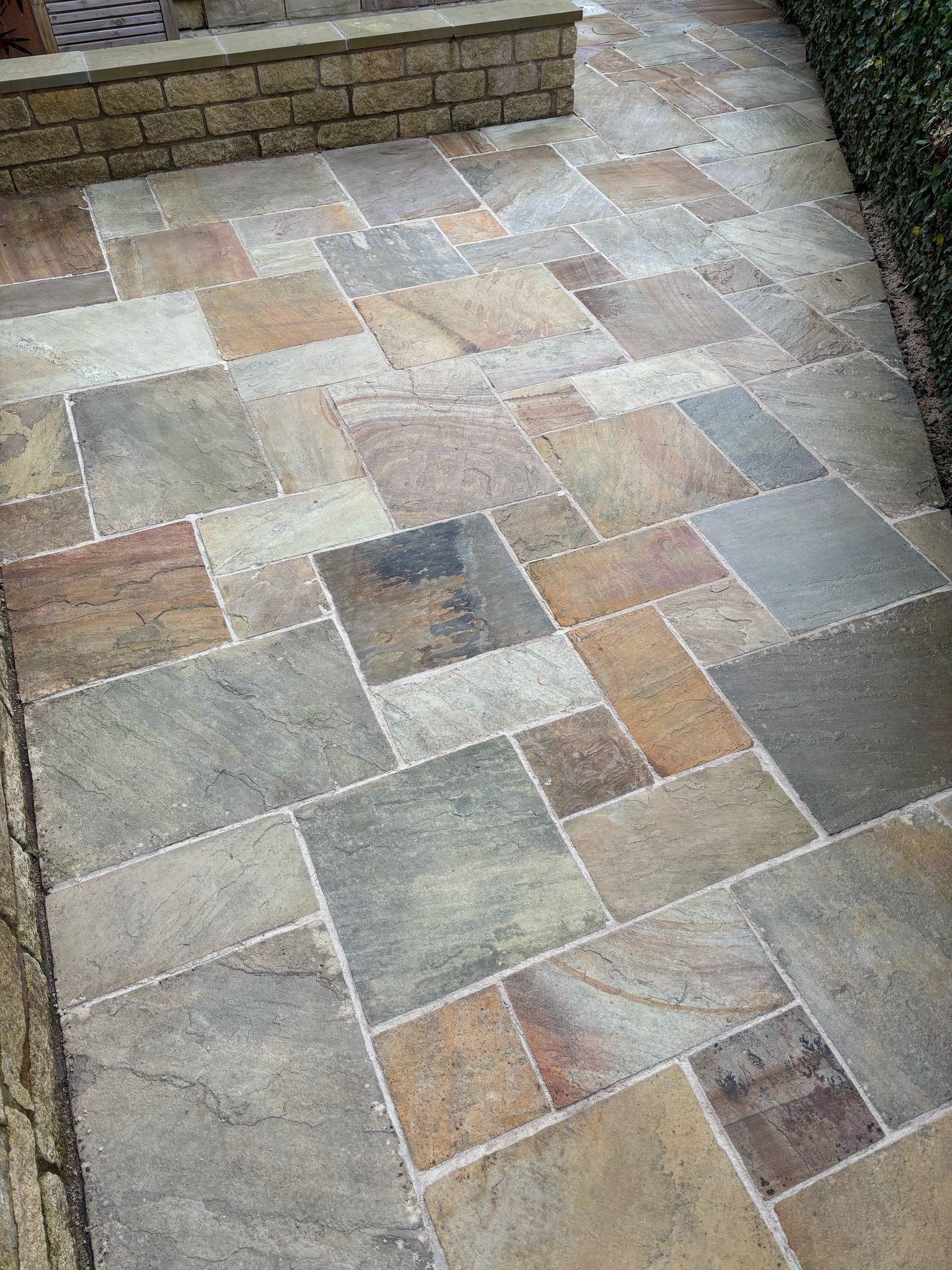 Stone-paved patio with multicolored rectangular pavers and a brick wall at the top edge