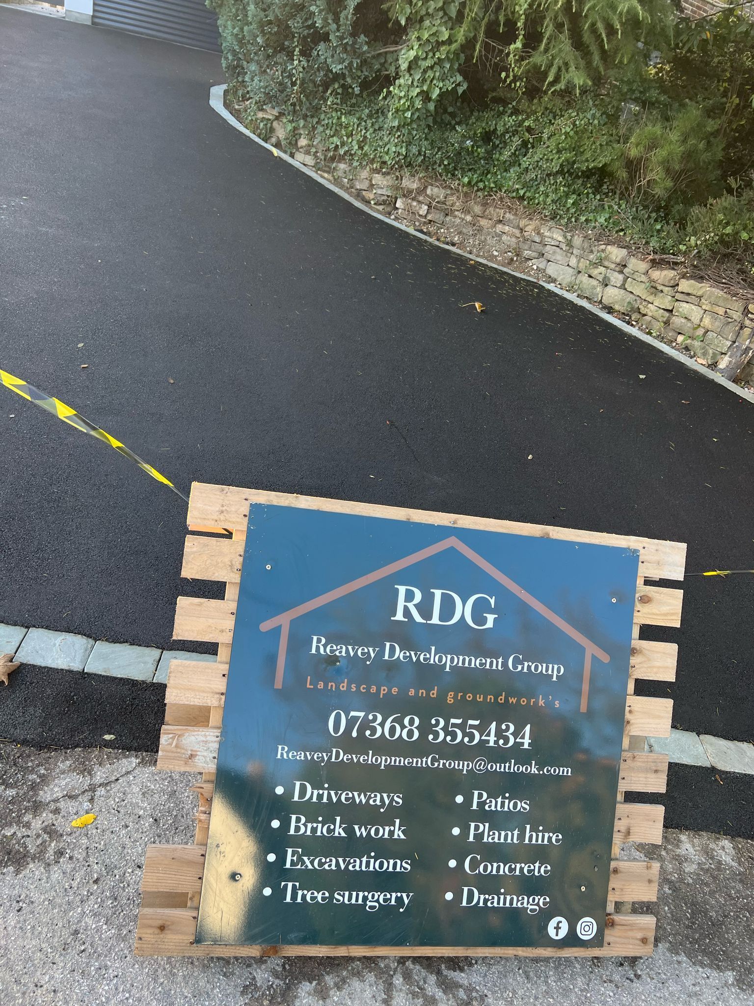 Blue RDG sign on a wet roadside beside a hedge and curved asphalt path