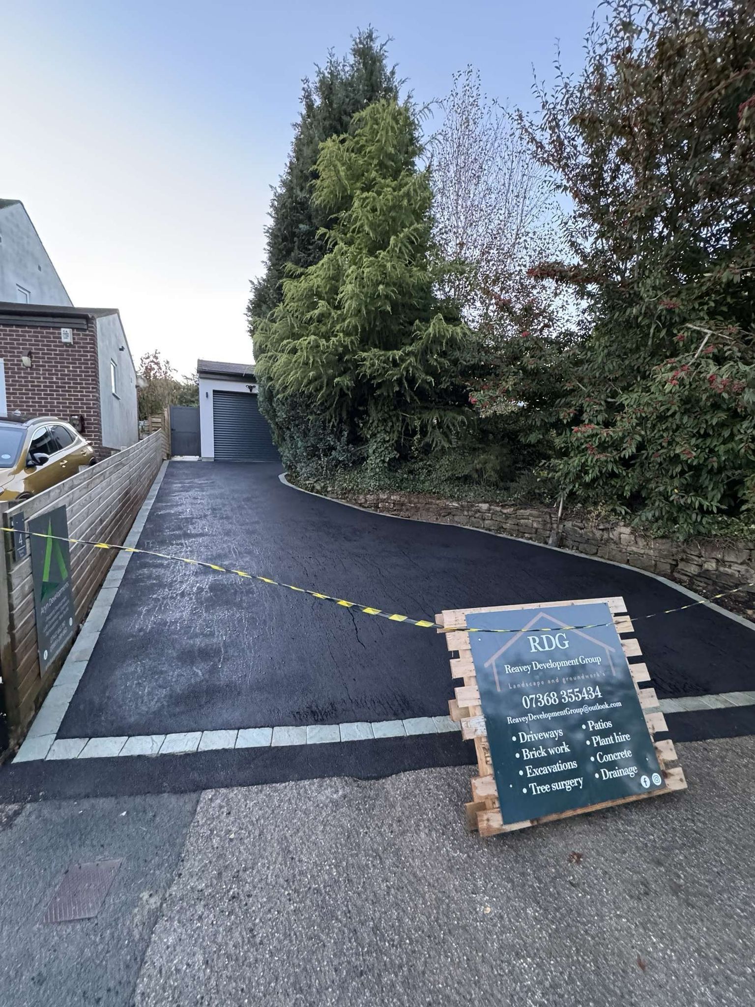 Outdoor driveway entrance with a chalkboard sign beside a hedge and fence.