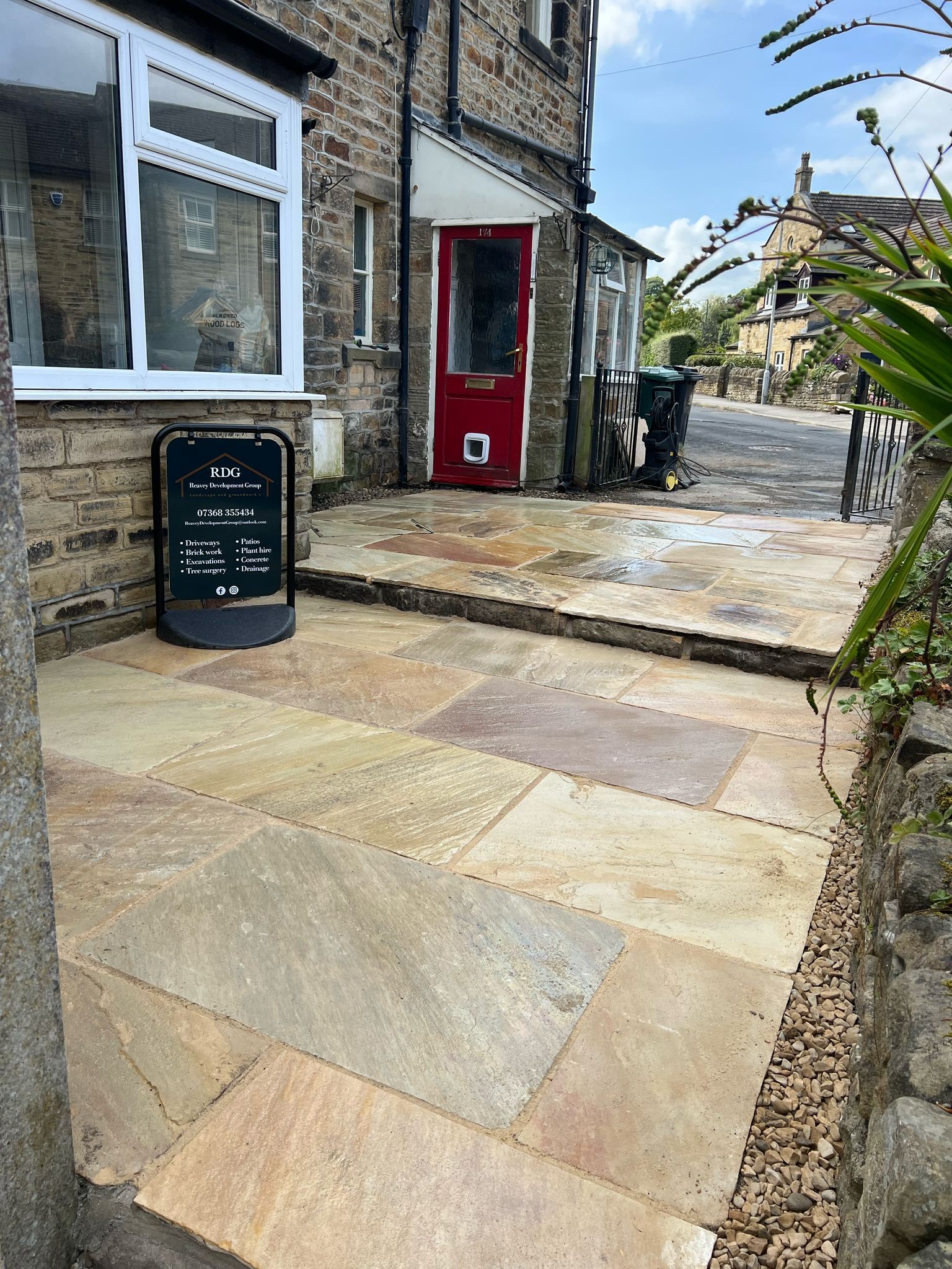 Stone-paved courtyard beside a rustic stone building with a red door and a black signboard.