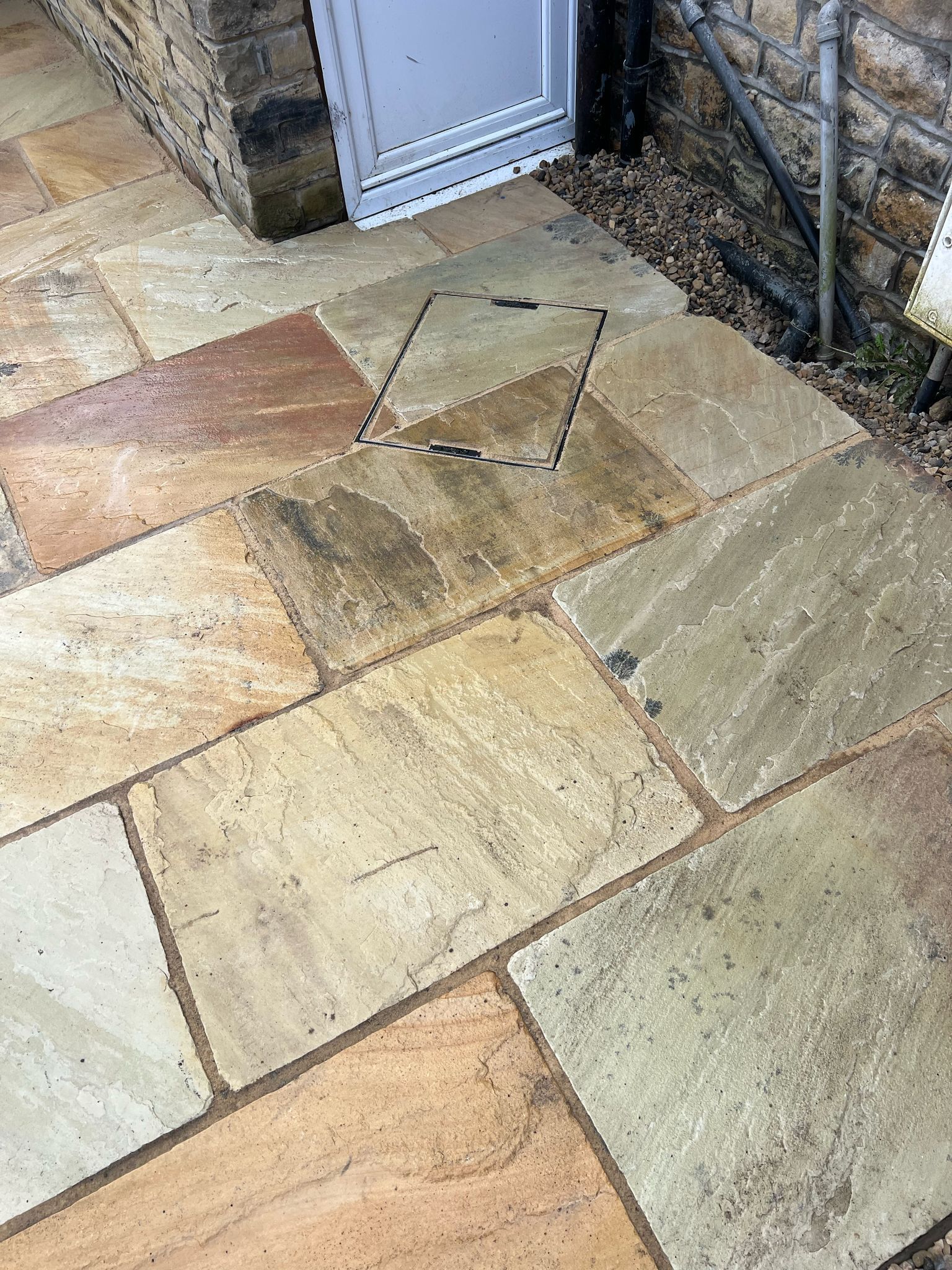 Stone patio with beige and tan paving slabs beside a white door and stone wall