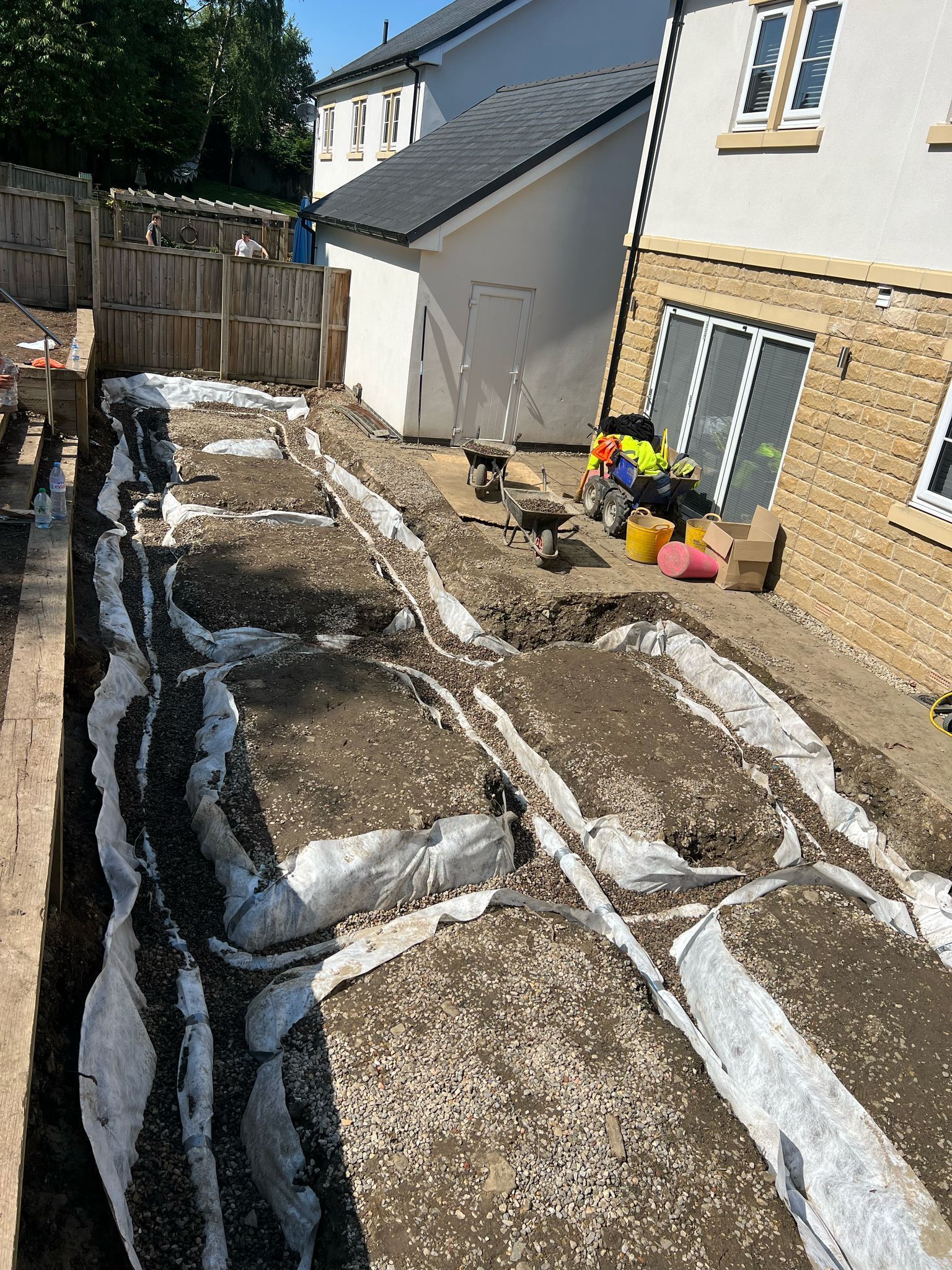 Backyard construction site with gravel trenches, white membrane strips, and a house wall on the right