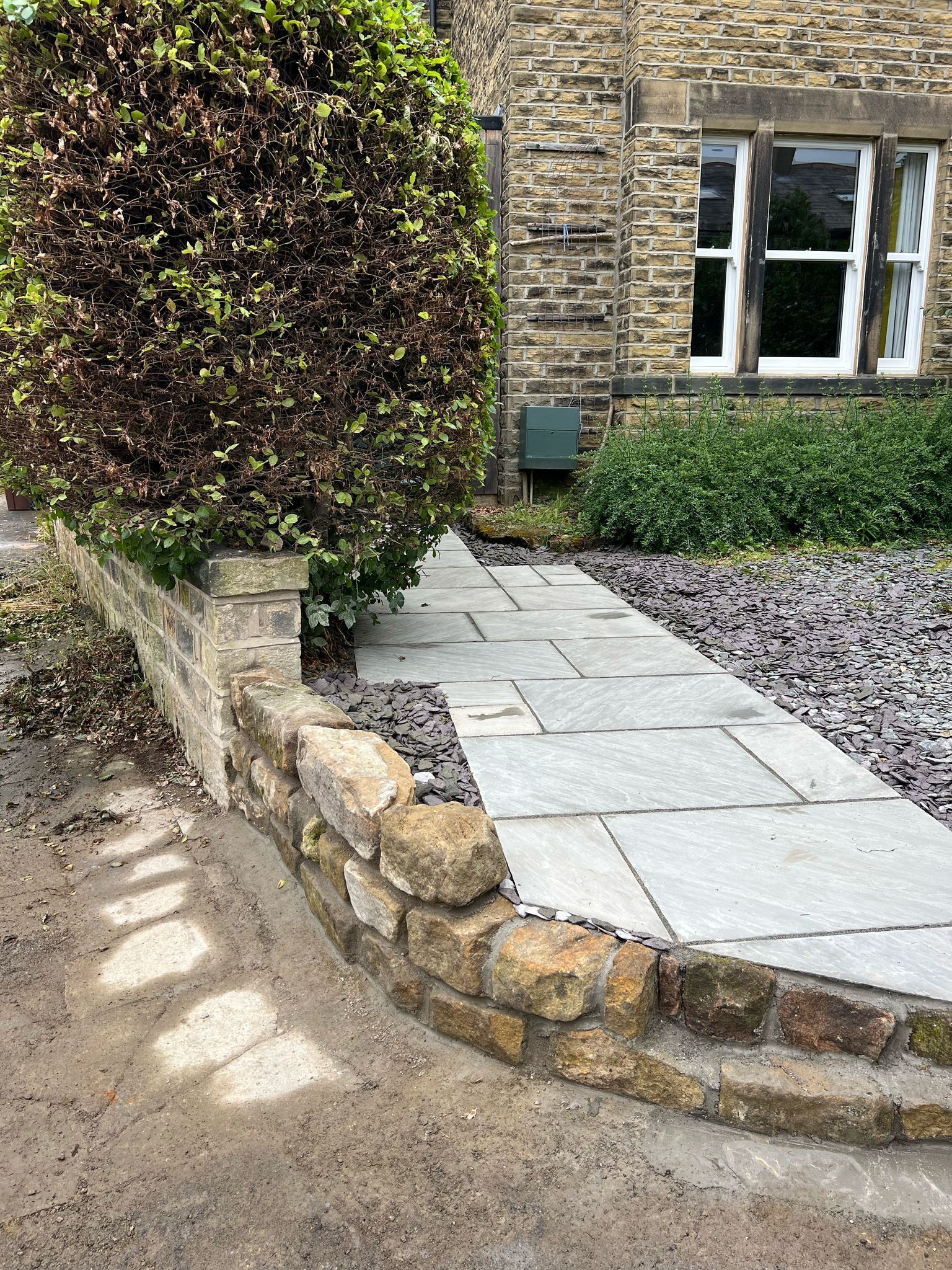 Stone garden steps beside a house with a hedge, paved path, and gravel border