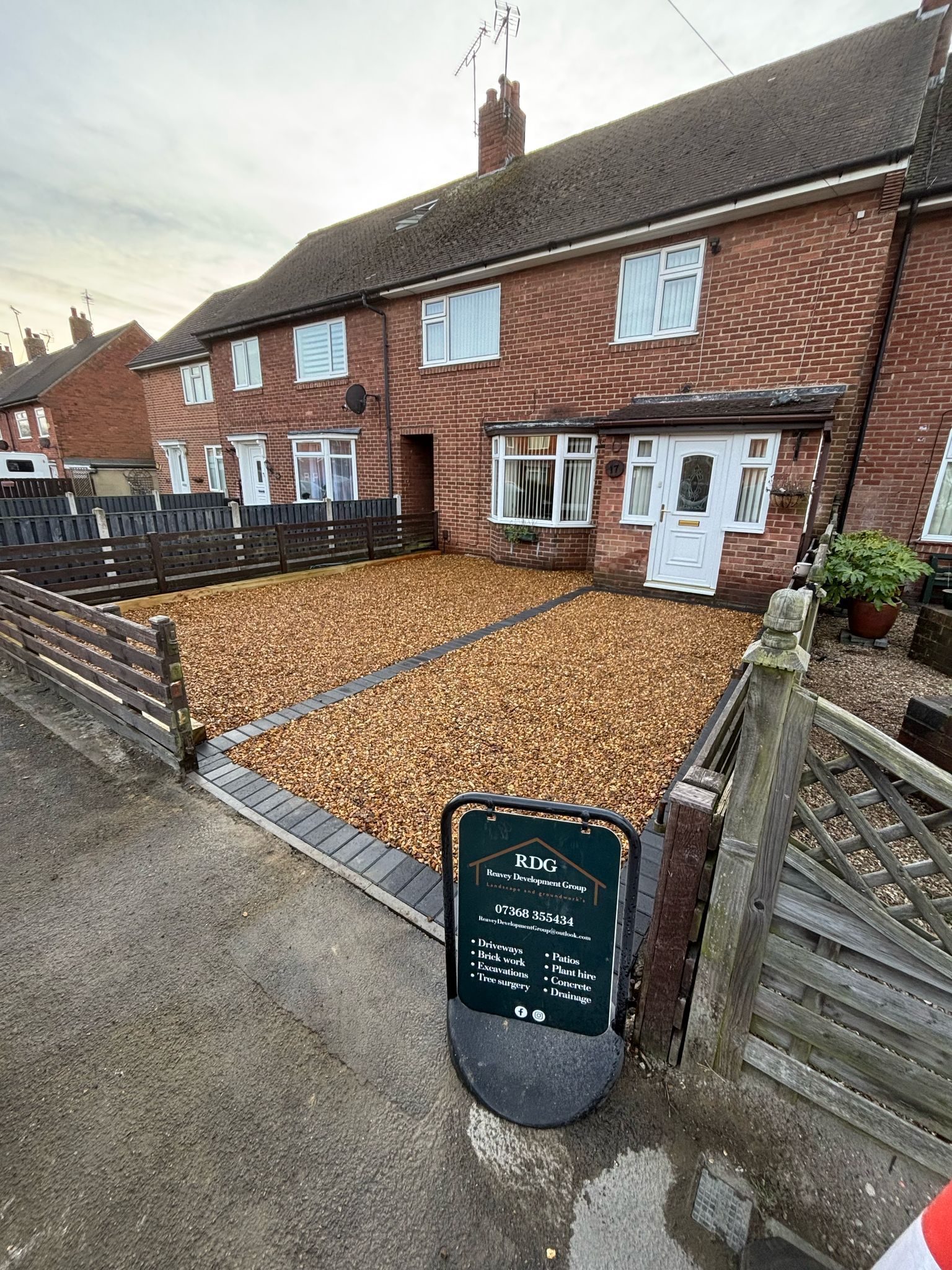 Terraced houses with pebble driveway, white front doors, and a small green sign by the gate