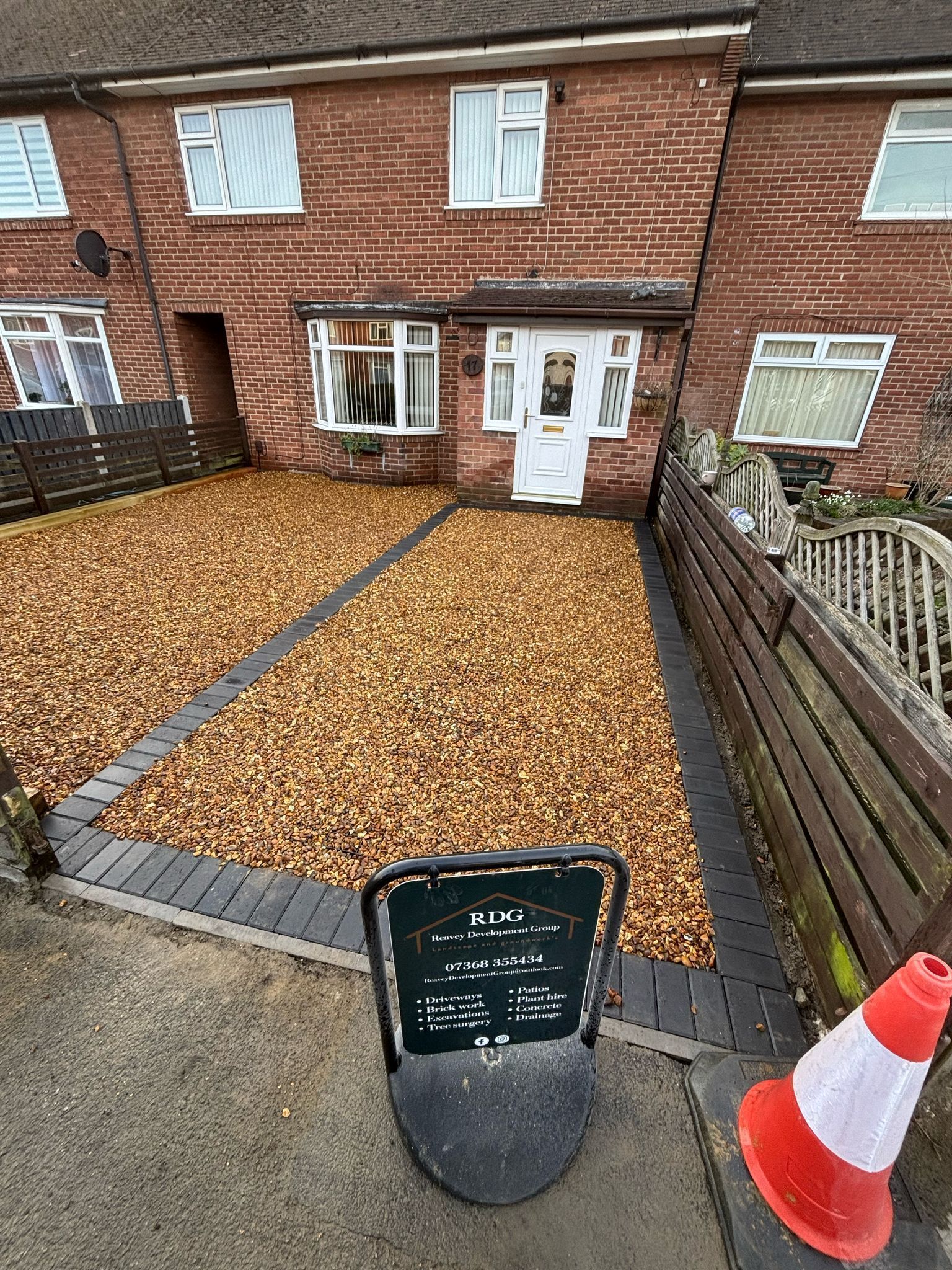 Front view of brick house with gravel driveway, white door, and orange traffic cone in foreground