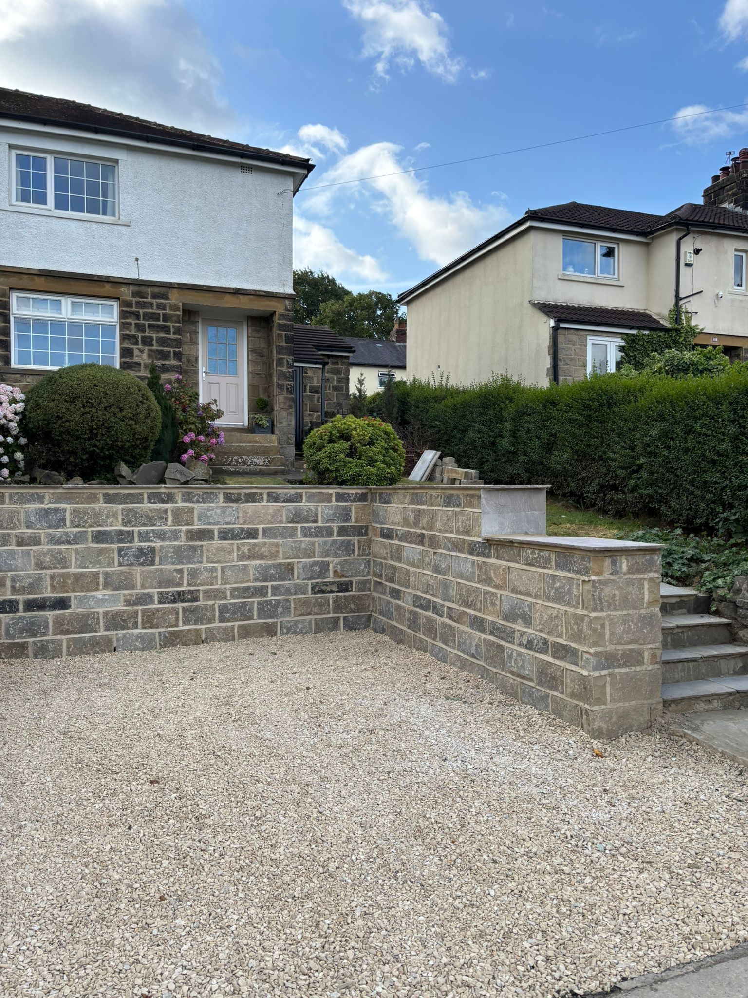 Gravel front yard with stone retaining walls and steps beside a gray house in a suburban neighborhood