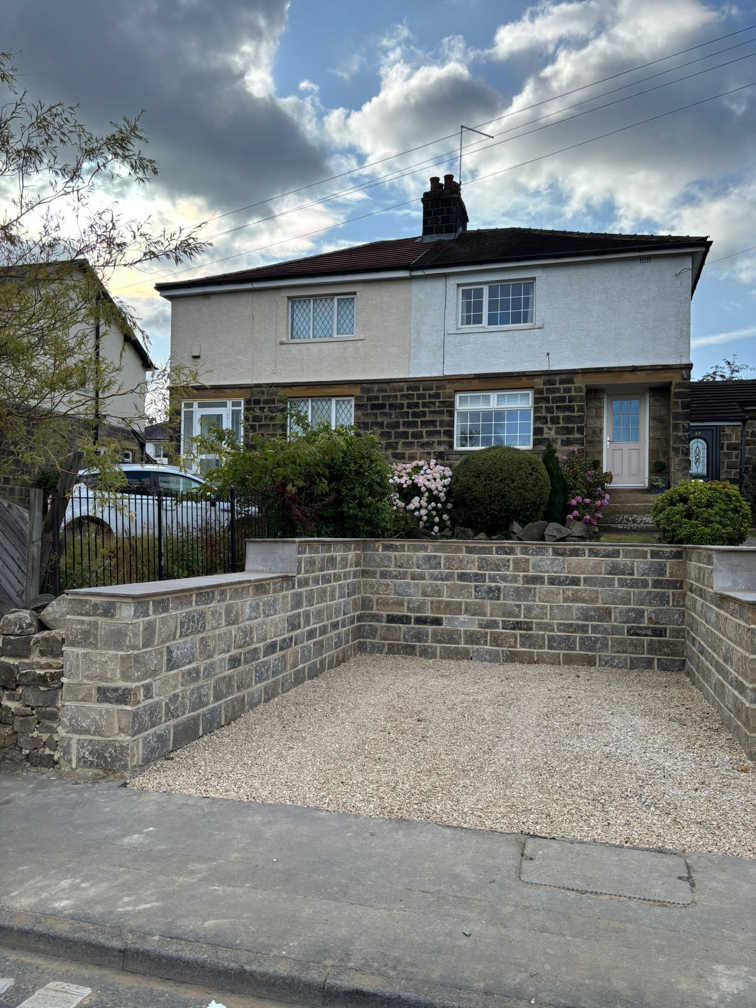 Semi-detached house with stone front wall, gravel driveway, and cloudy sky