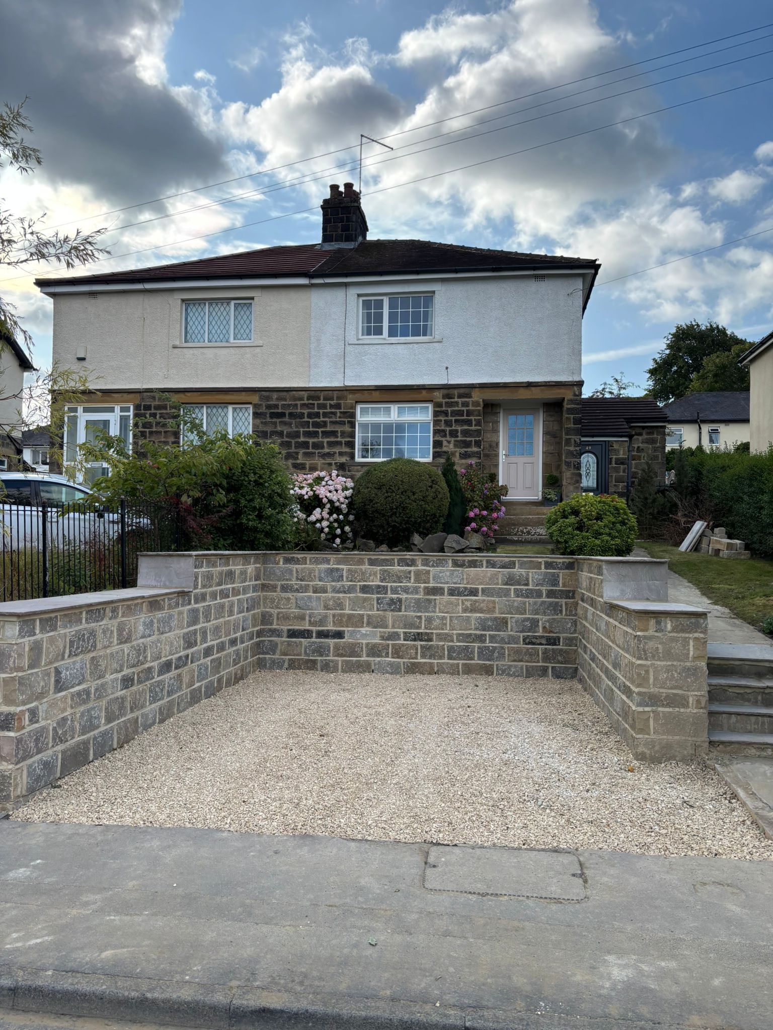 Semi-detached house with low stone wall and gravel driveway under a cloudy sky
