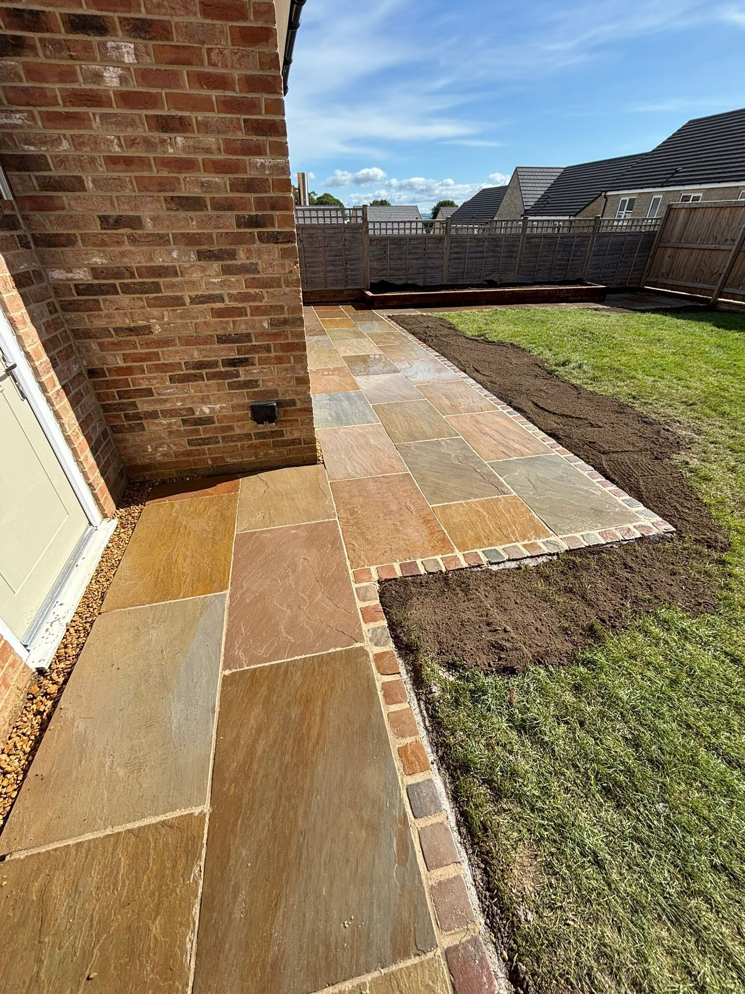 Stone patio beside a brick wall and grassy yard under a clear blue sky
