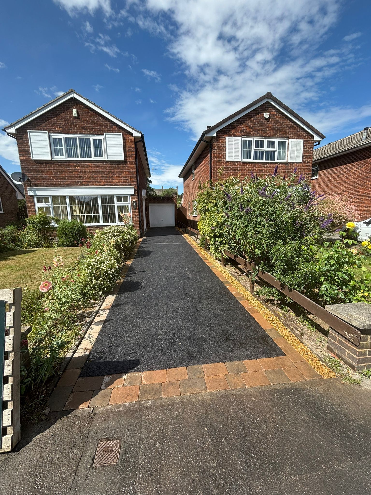 Two brick houses with gravel driveway, front gardens, and blue sky on a sunny day