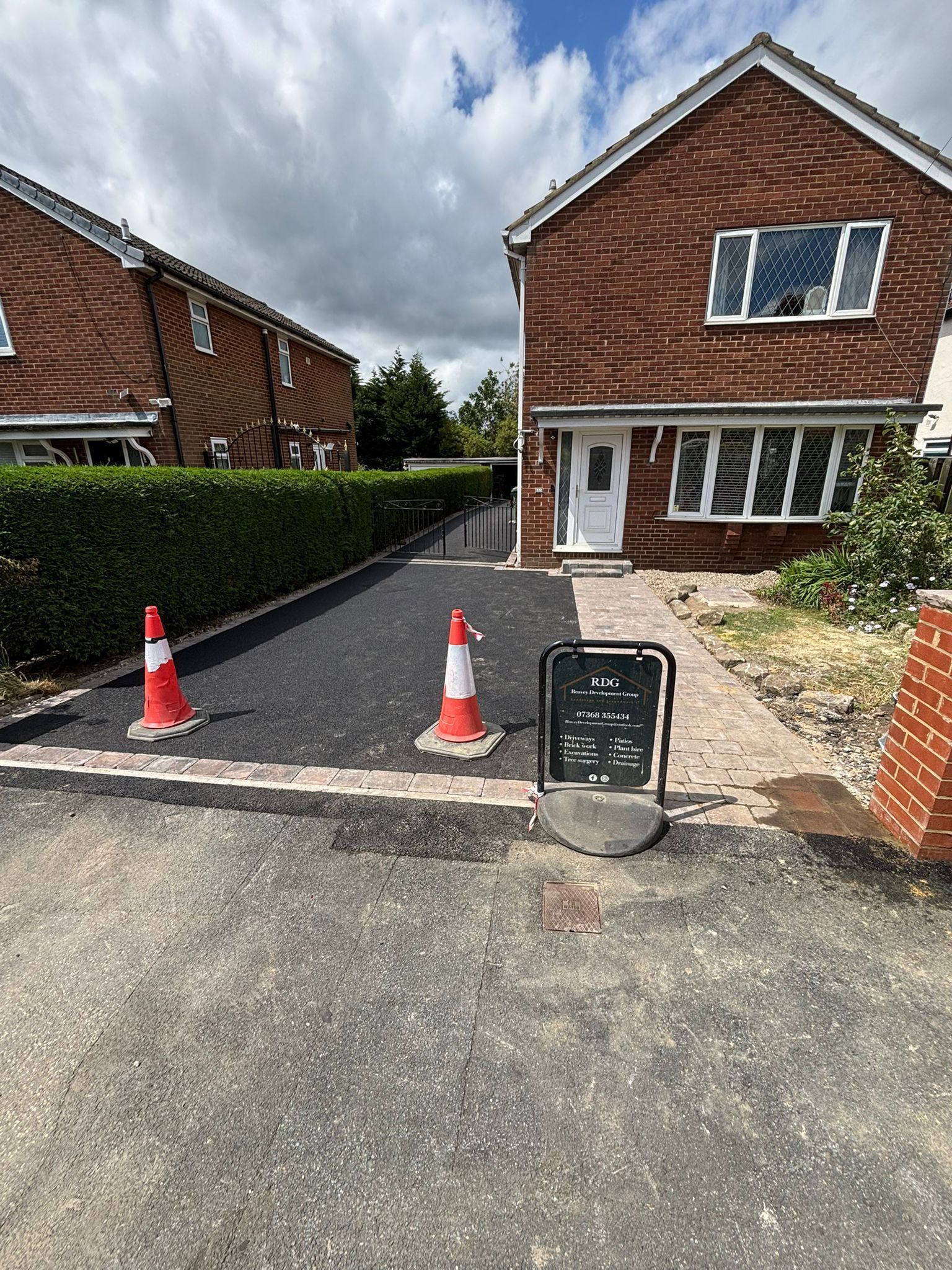 Driveway entrance to a red-brick house with traffic cones and a sign blocking access