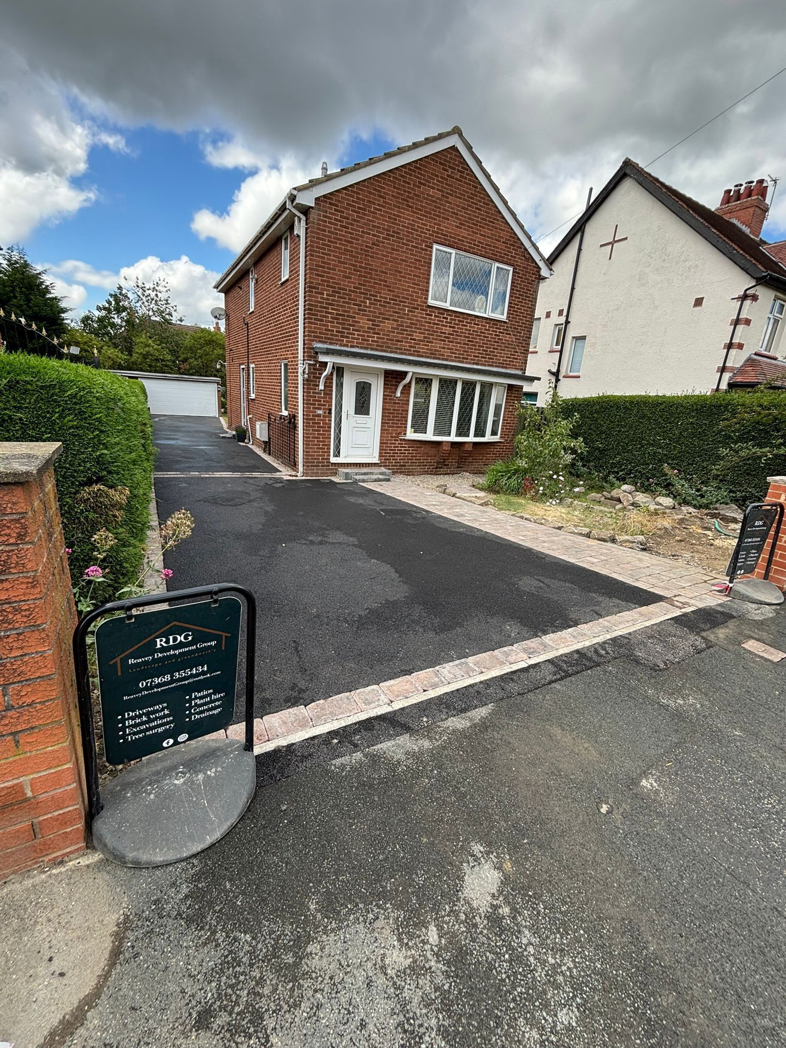 Suburban brick house with driveway, hedge, and a chalkboard sign by the gate