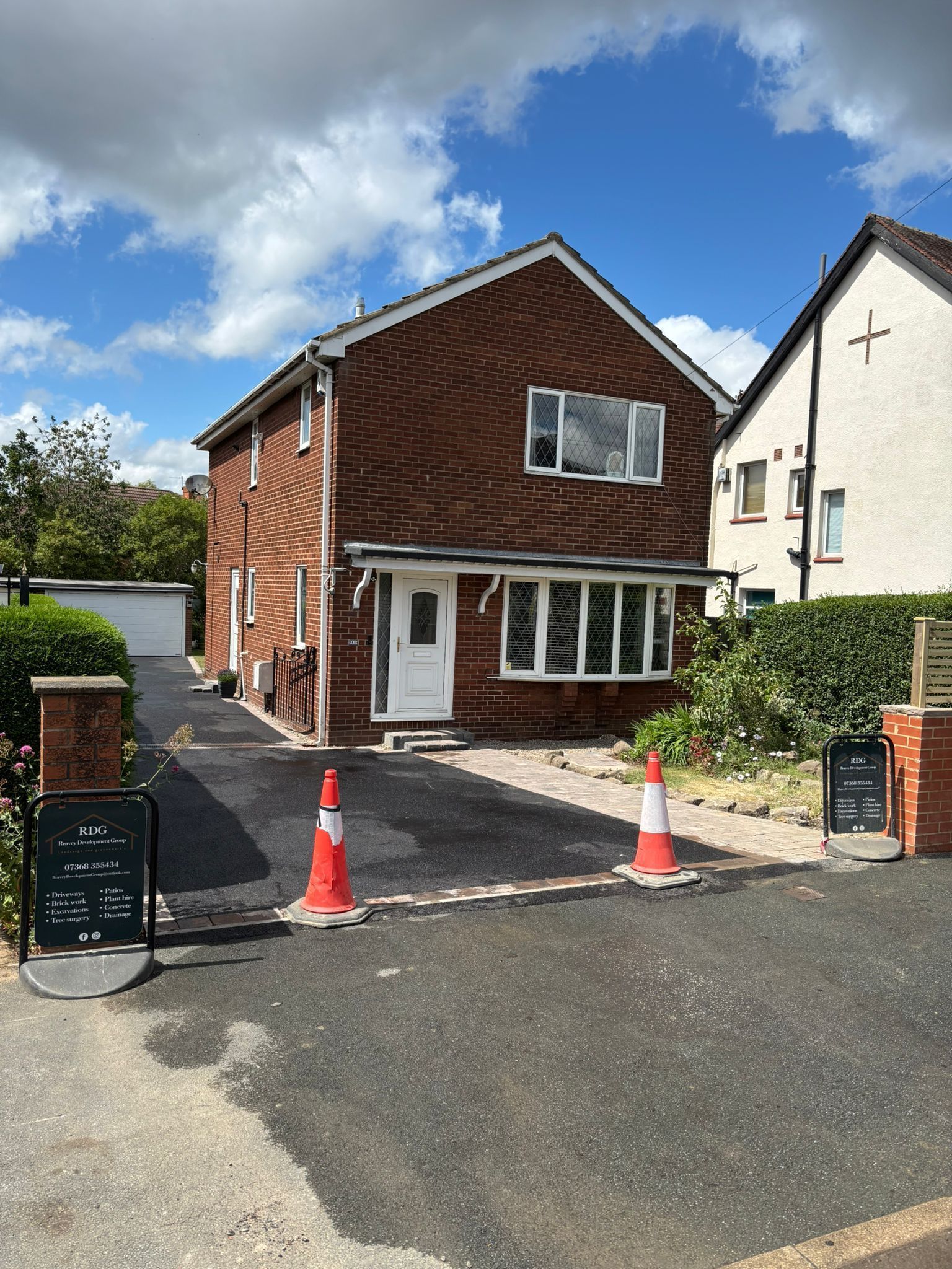 Small brick house with white trim, driveway, and two orange traffic cones under a bright blue sky