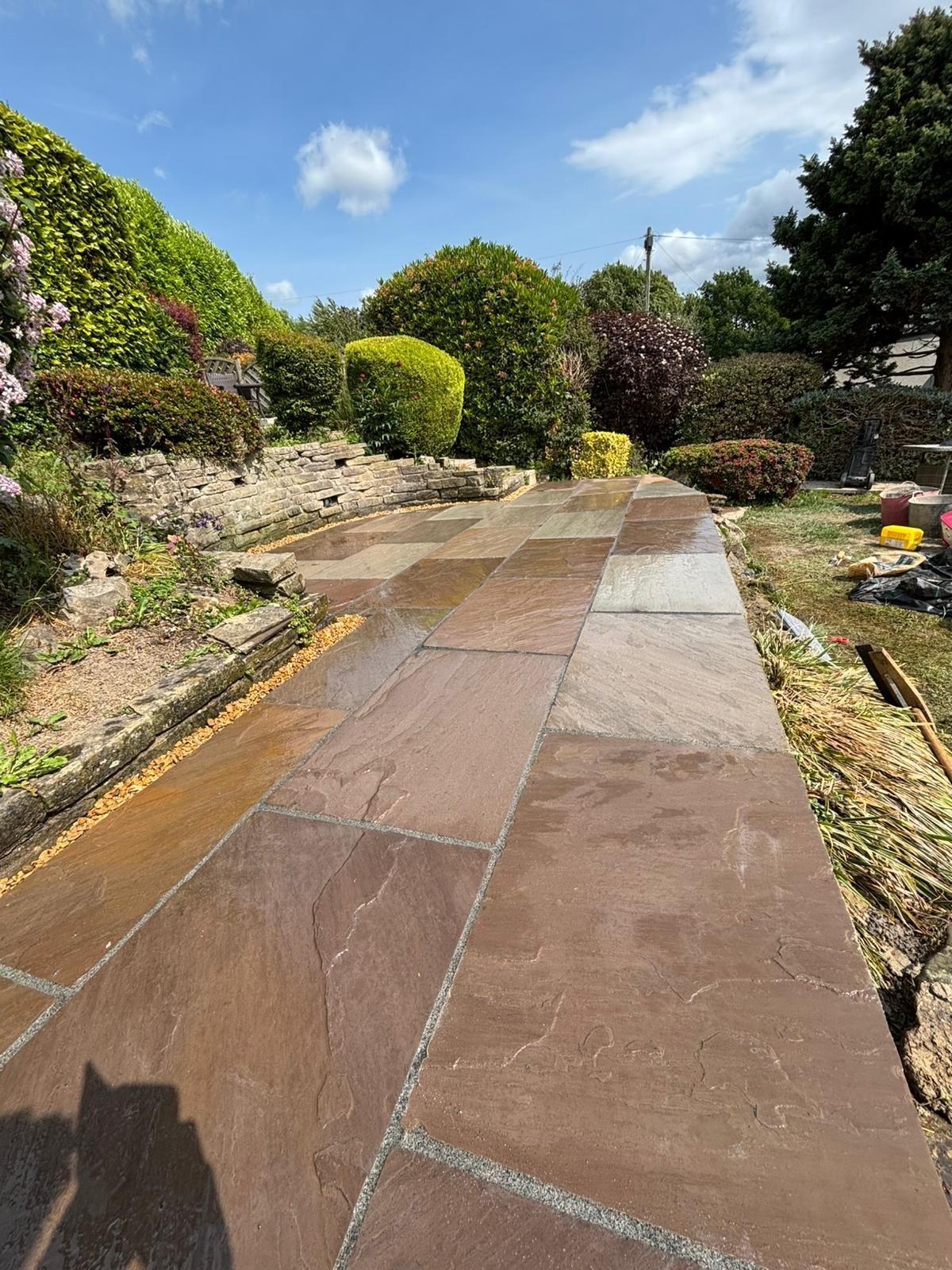 Stone garden path lined with shrubs and flowers under a bright blue sky