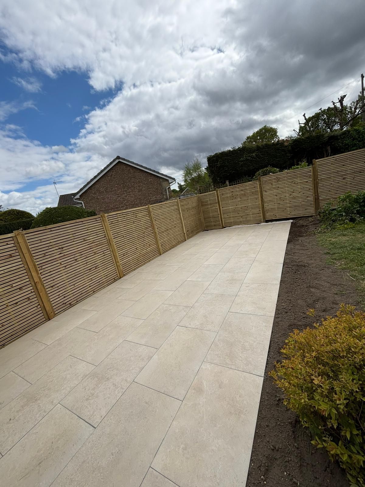Curved concrete driveway beside a wooden fence under a cloudy sky