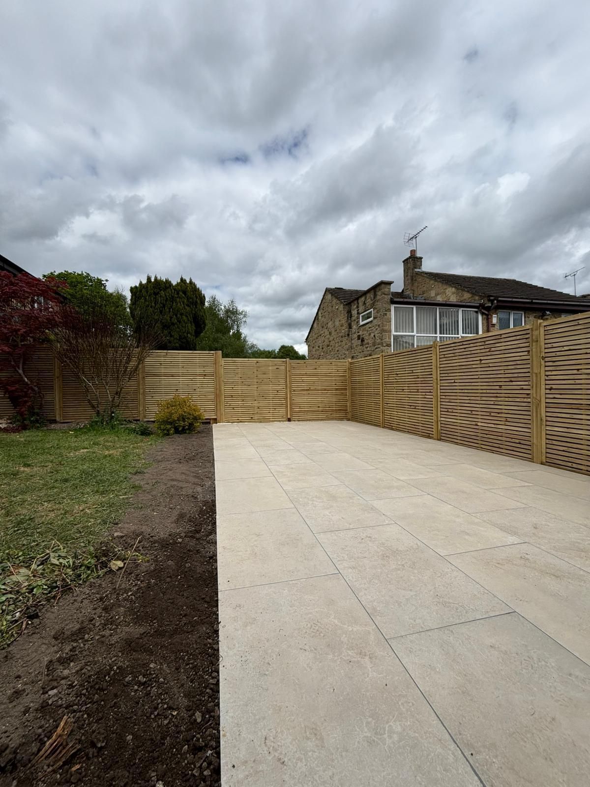 Concrete driveway leading to a wooden gate beside a house under a cloudy sky