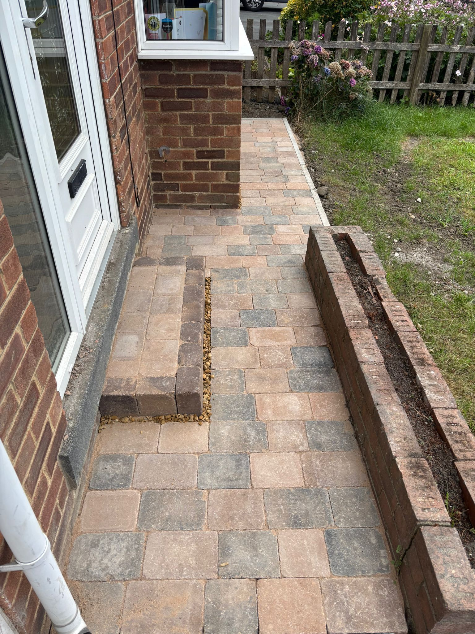 Brick patio beside house entrance with low retaining walls and a narrow walkway, showing a small step up.