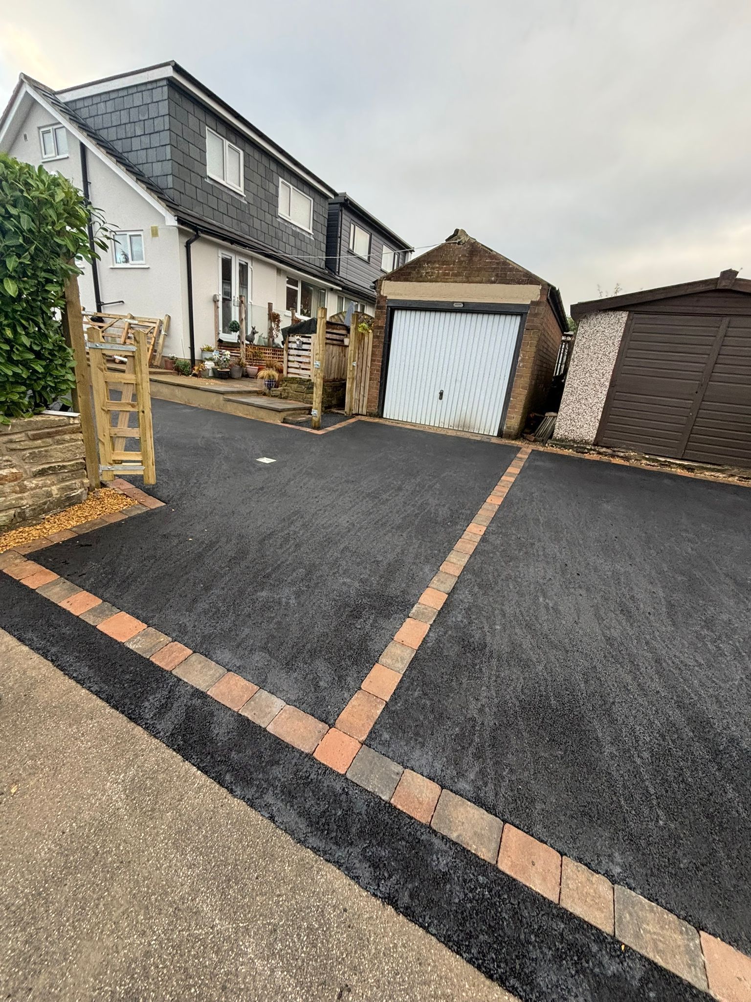 Driveway with black resurfacing and orange edging beside a white house and garage.