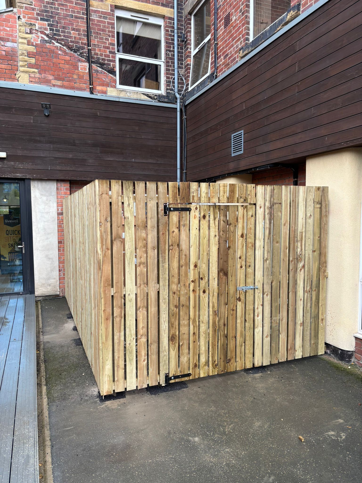Wooden storage enclosure beside a brick building in a narrow alleyway