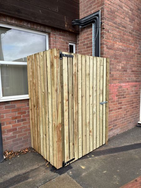 Wooden outdoor storage enclosure beside a brick building on pavement