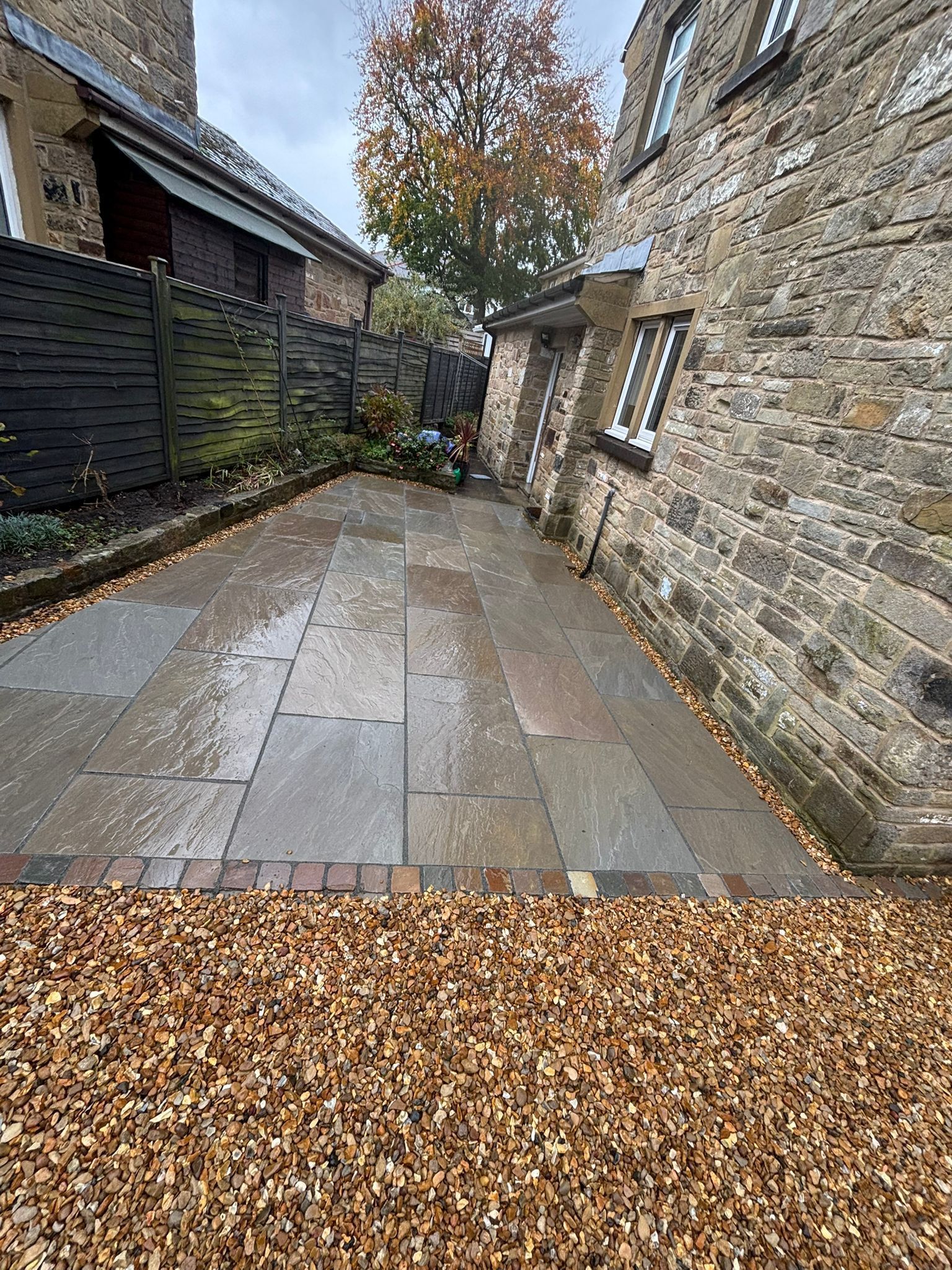 Narrow stone courtyard with wet paving, fallen leaves, and a stone building wall