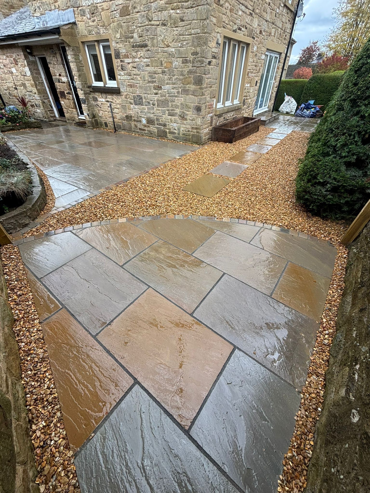 Stone walkway and gravel path leading to a house entrance, bordered by shrubs.