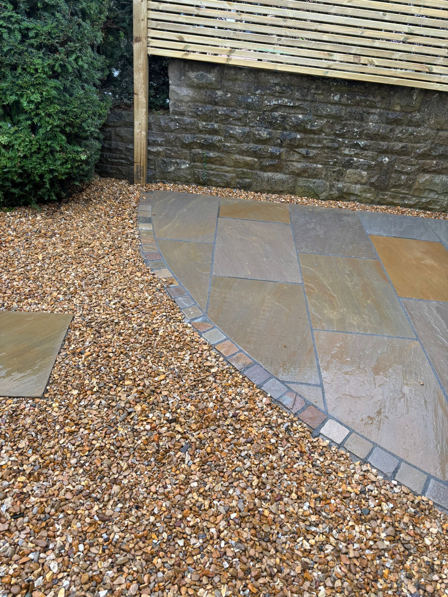 Gravel and slate patio beside a stone wall and hedge in a landscaped garden