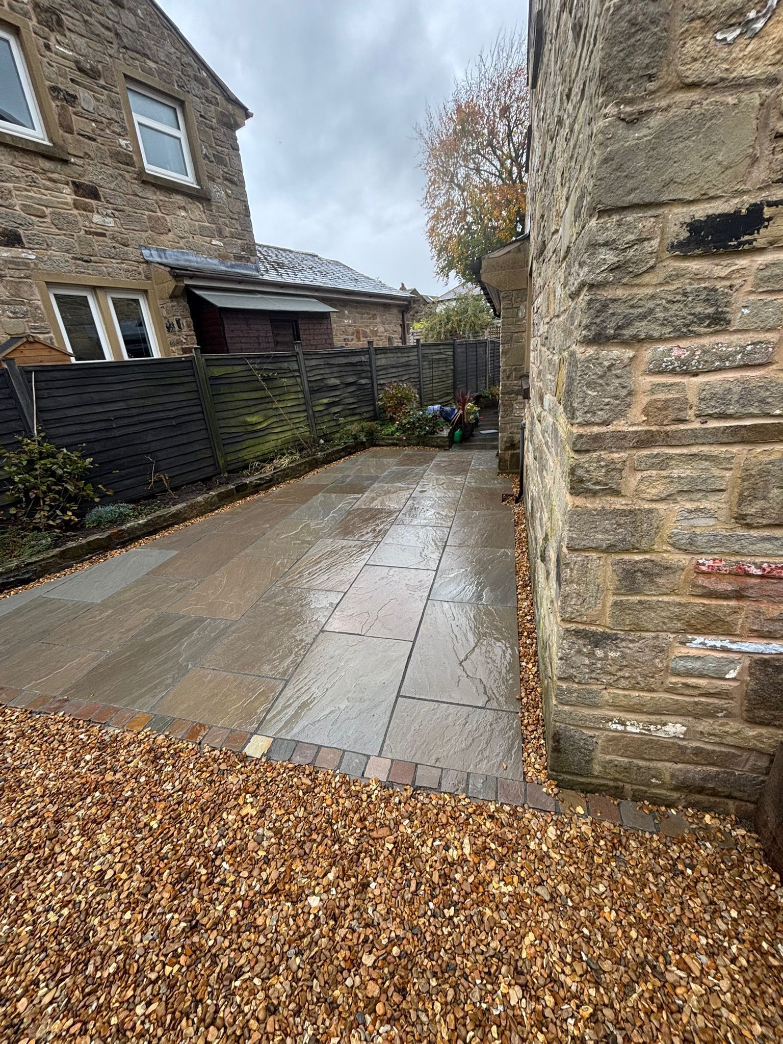 Wet stone courtyard beside stone houses, with fallen leaves and a small garden wall.