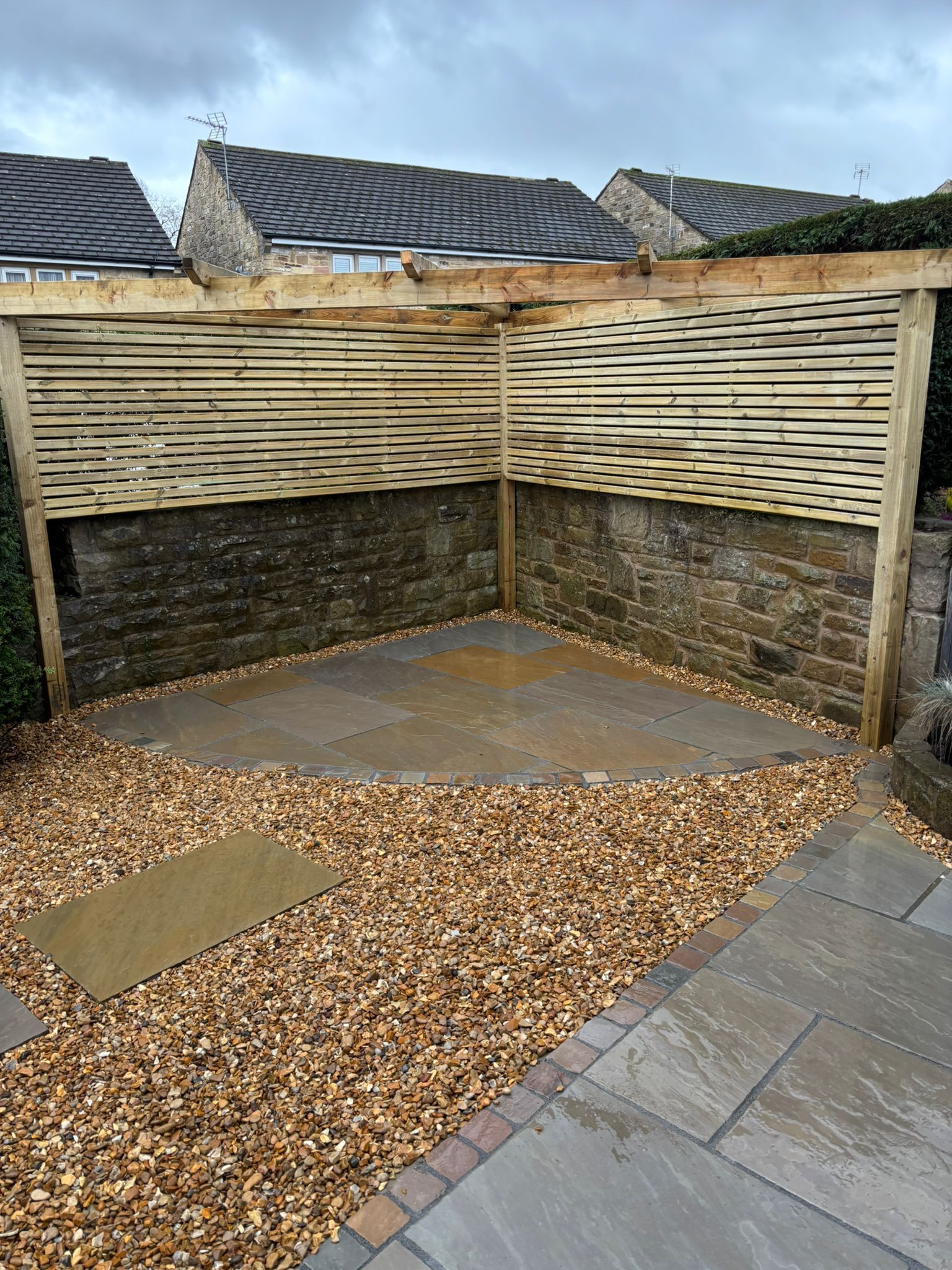 Small backyard patio with gravel, paved tiles, and a wooden privacy fence under overcast skies