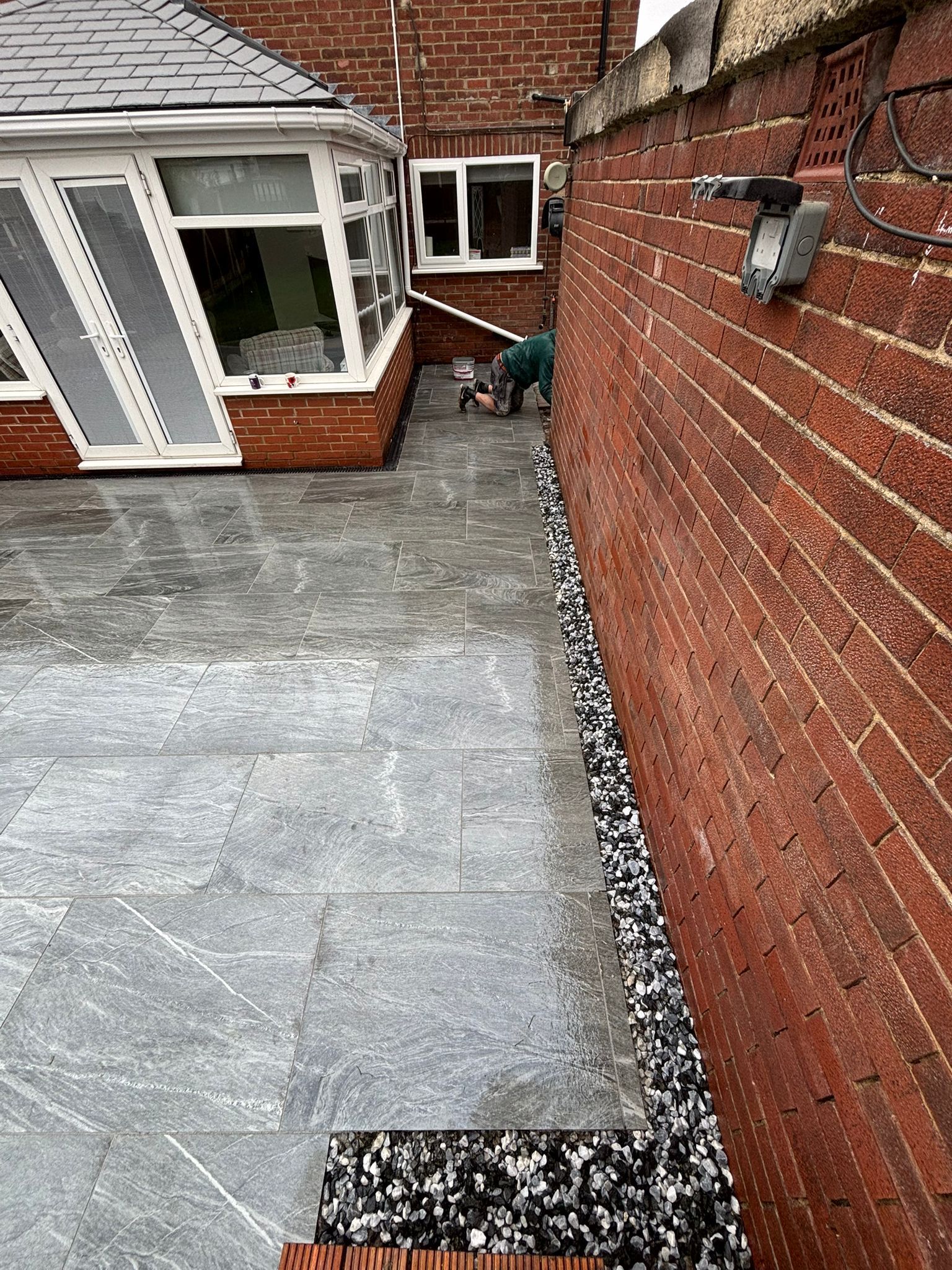 Brick patio beside house windows and a red brick wall, with a small dog near the far end.