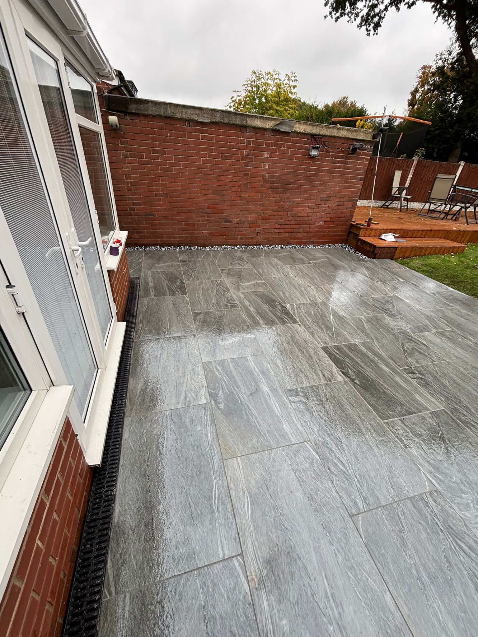 Patio with gray concrete floor beside a brick wall and house siding, viewed from a doorway
